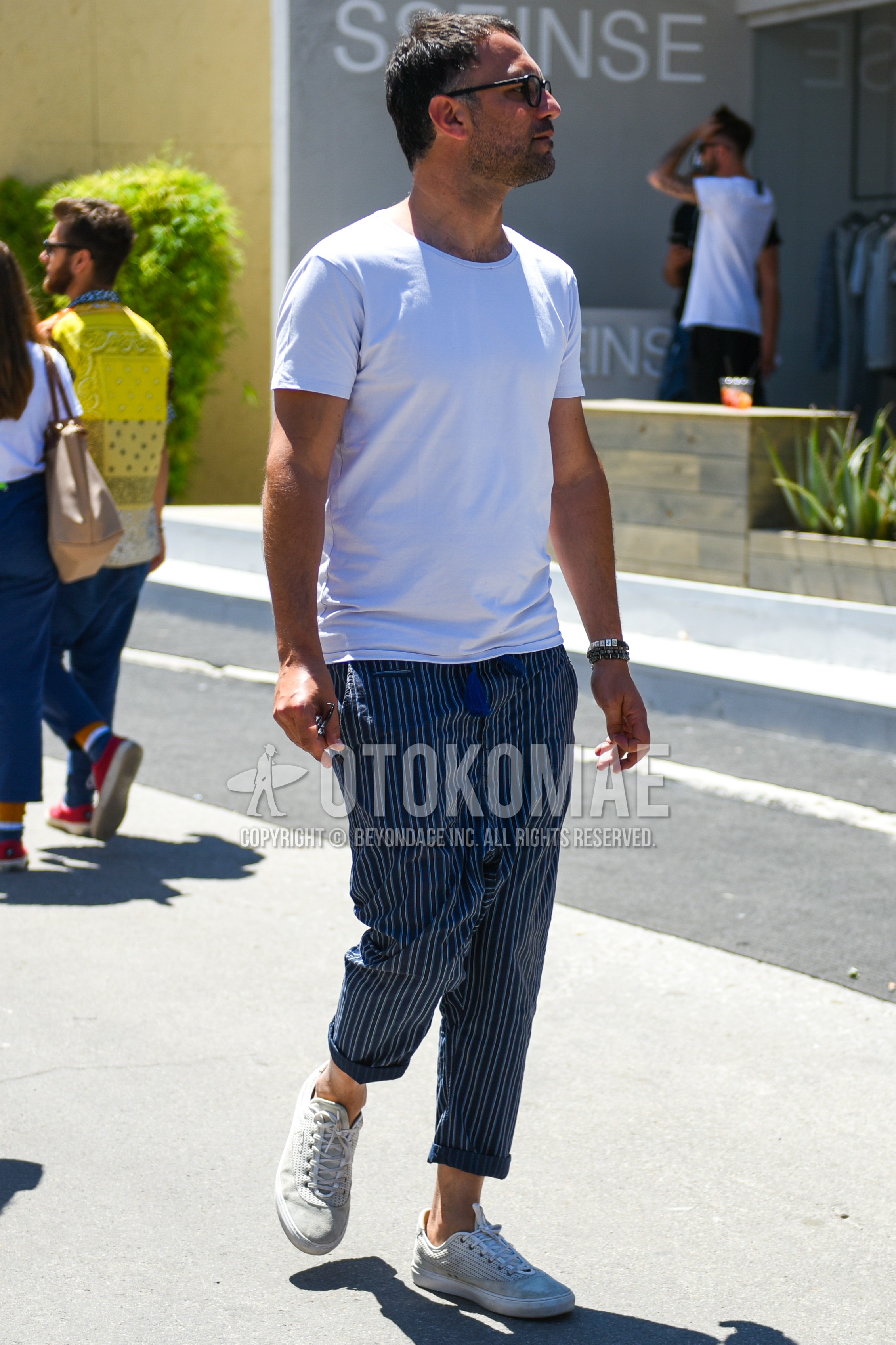 Men's summer outfit with black plain glasses, white plain t-shirt, blue stripes easy pants, white low-cut sneakers.