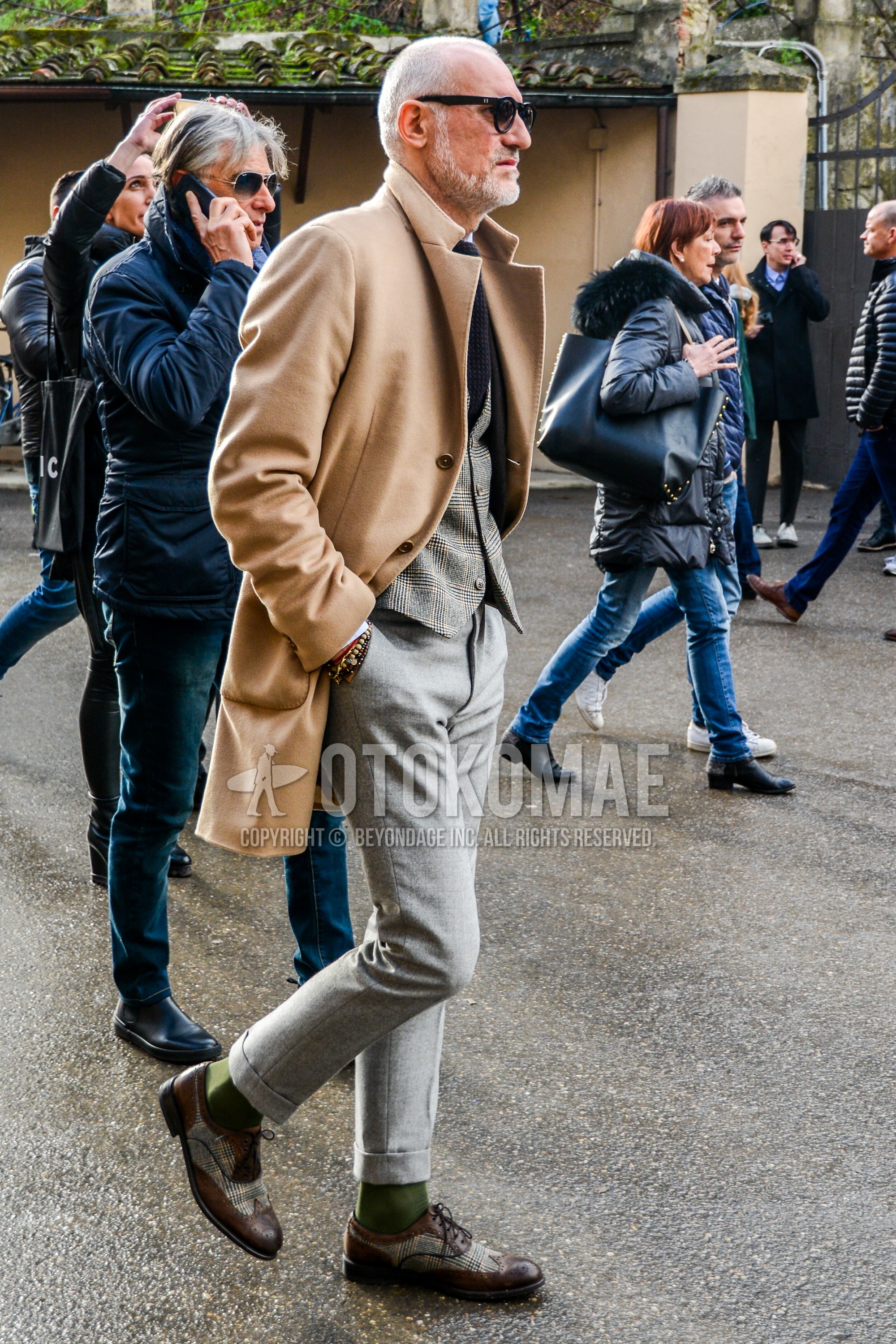 Men's winter outfit with plain sunglasses, brown plain chester coat, gray check gilet, gray plain slacks, olive green plain socks, brown brogue shoes leather shoes, black plain knit tie.