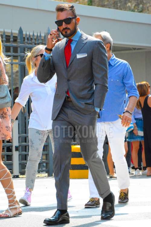 黒無地のサングラス、ブルー無地のシャツ、ブラウン無地のレザーベルト、黒無地のソックス、黒ローファーの革靴、グレー無地のスーツ、レッドネクタイのネクタイを合わせた春秋のメンズコーデ・着こなし。