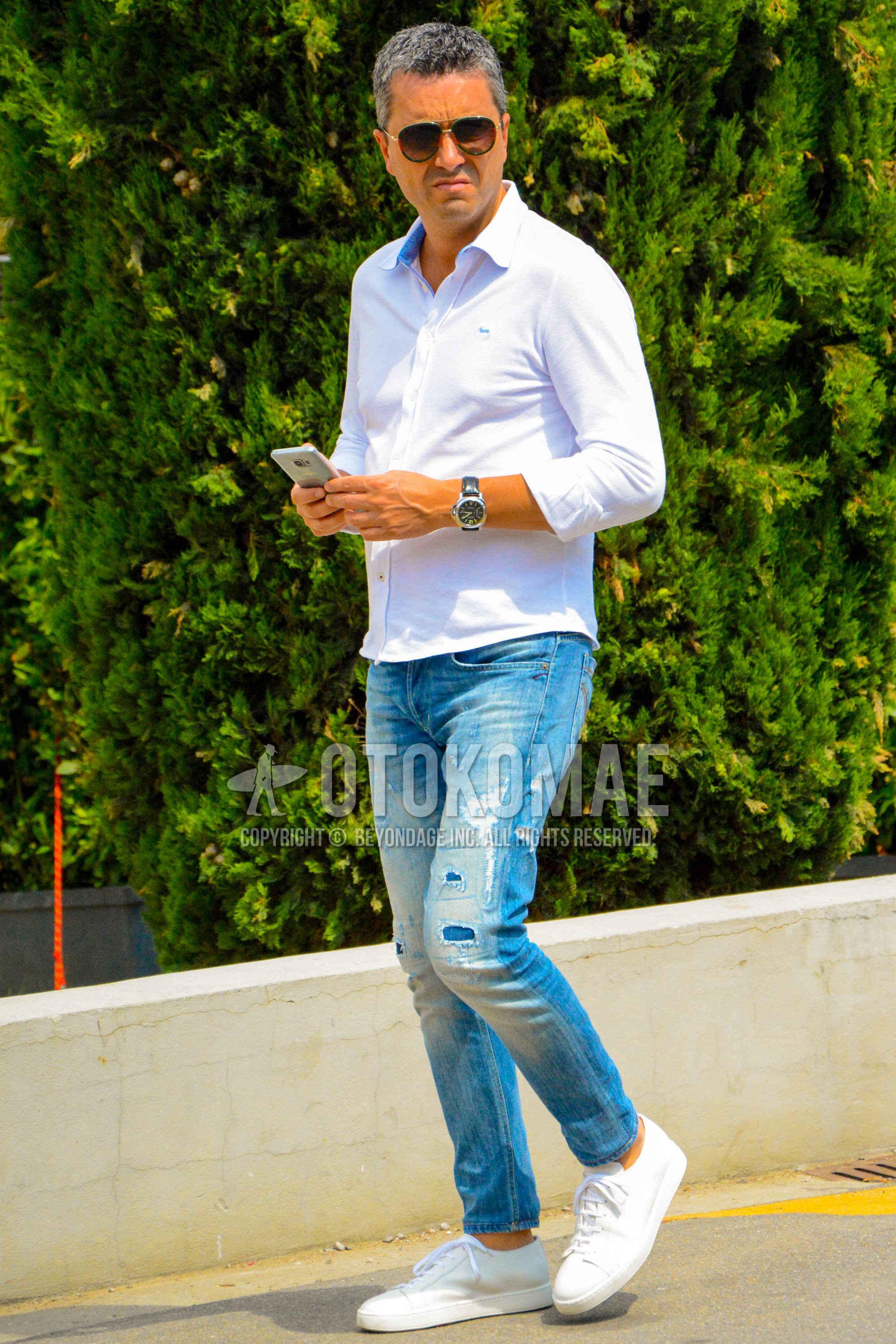 Men's spring summer outfit with green plain sunglasses, white plain shirt, blue plain damaged jeans, white low-cut sneakers.