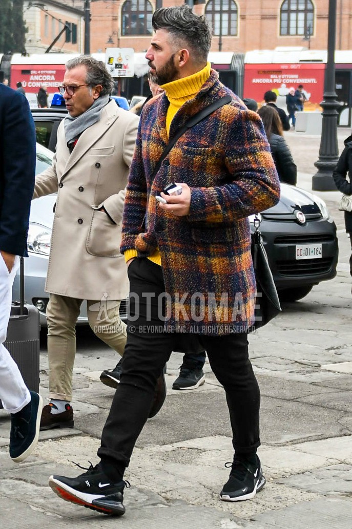 Men's autumn winter outfit with multi-color check chester coat, yellow plain turtleneck knit, black plain denim/jeans, black plain socks, black low-cut sneakers.