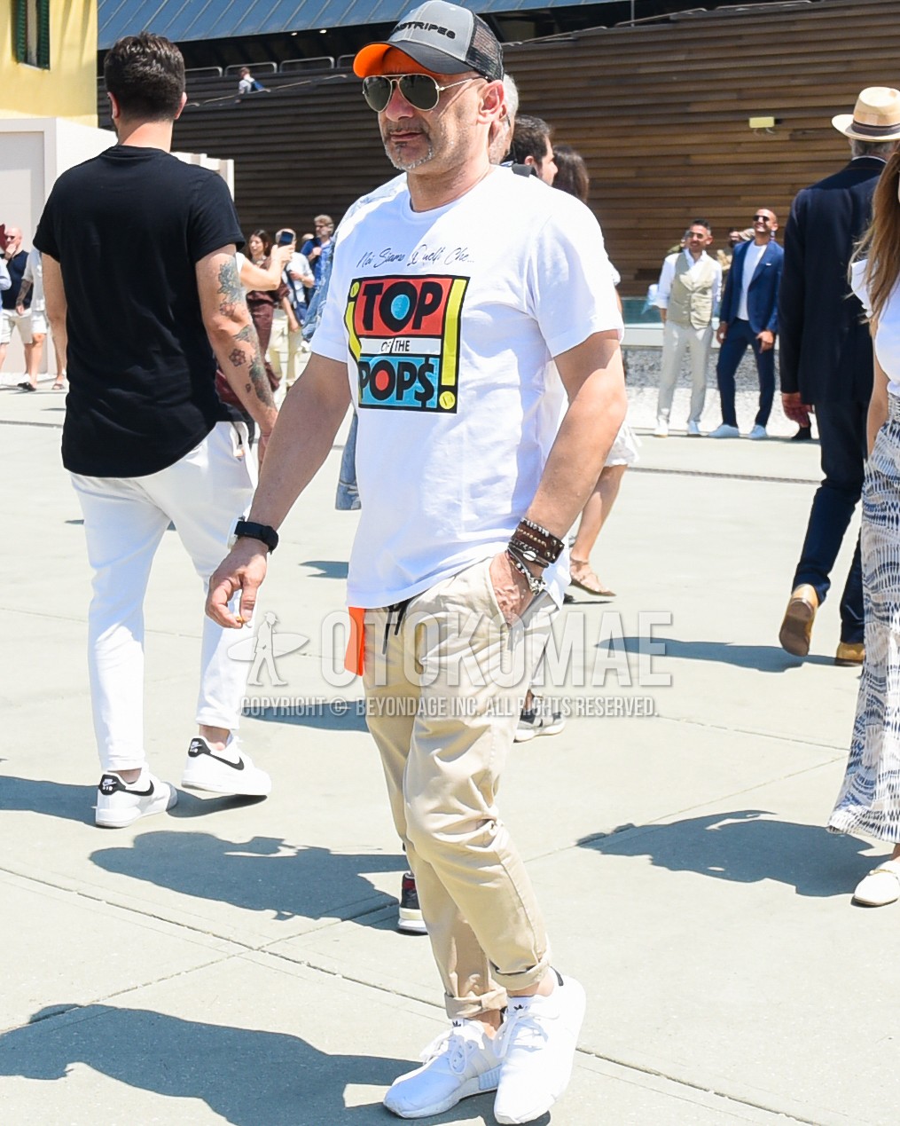 Men's spring summer outfit with gray deca logo baseball cap, black plain sunglasses, white graphic t-shirt, beige plain easy pants, white low-cut sneakers.