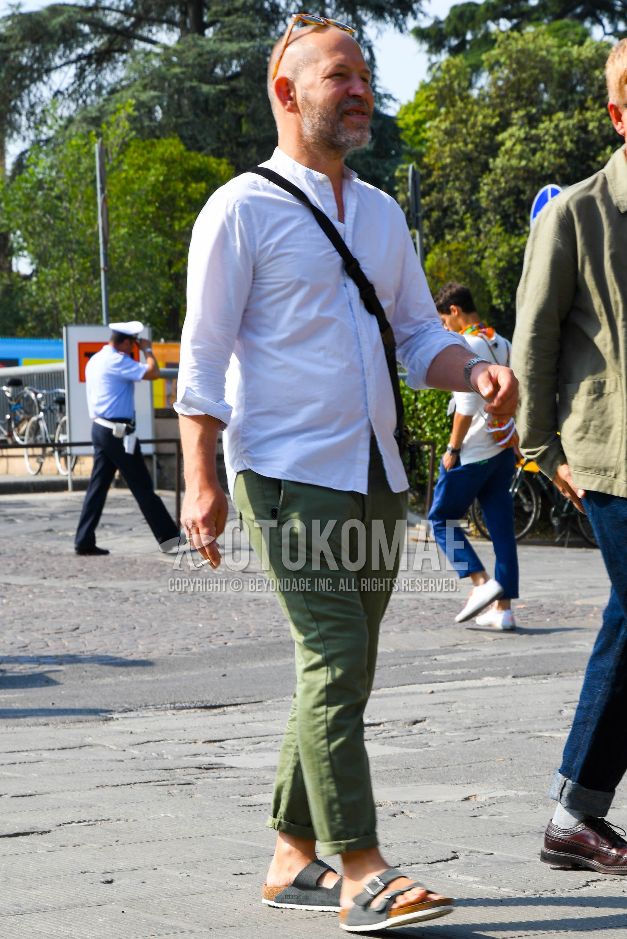 Men's summer outfit with white plain shirt, olive green plain chinos, black leather sandals.