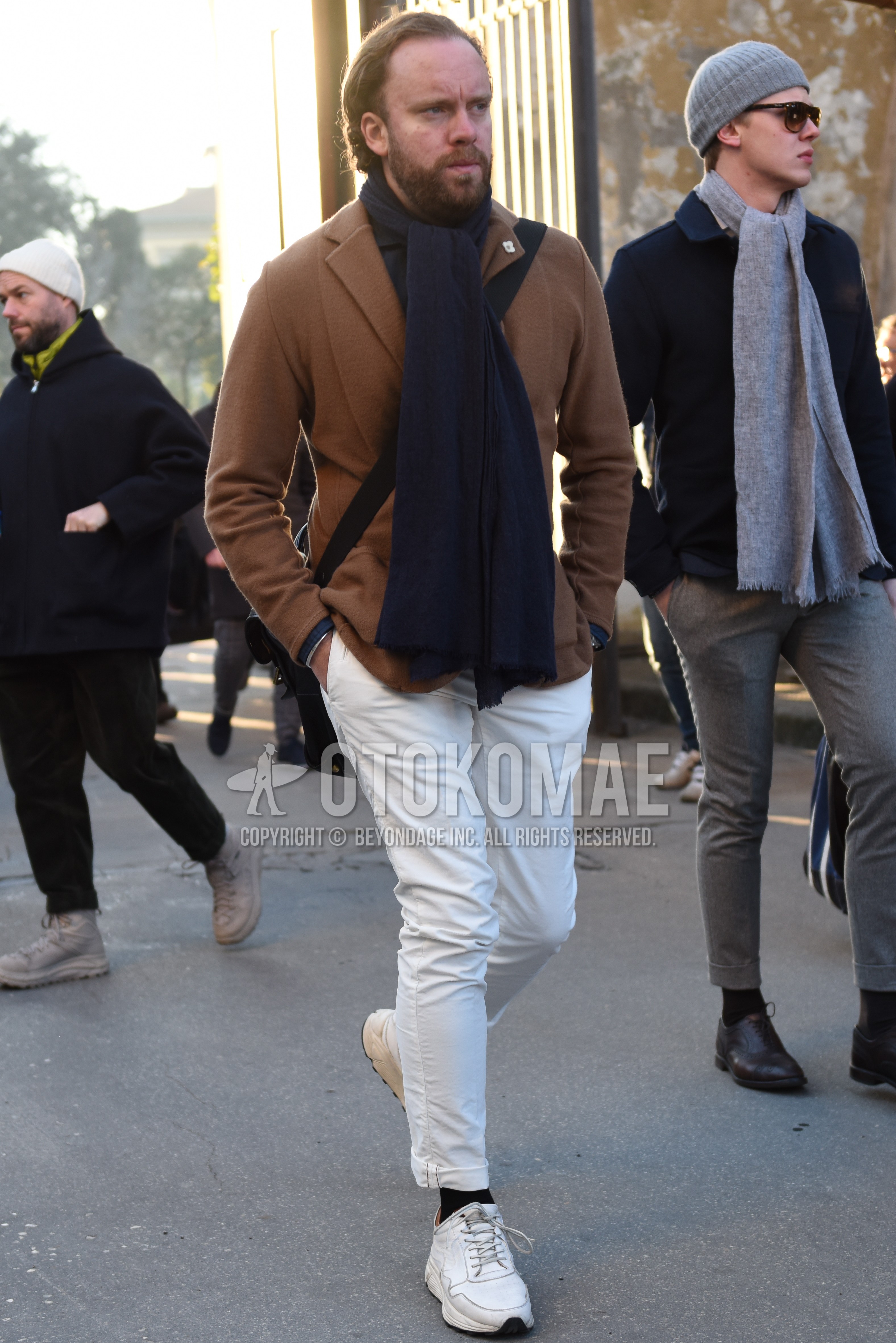 Men's autumn winter outfit with gray plain scarf, beige plain tailored jacket, white plain cotton pants, black plain socks, white low-cut sneakers.