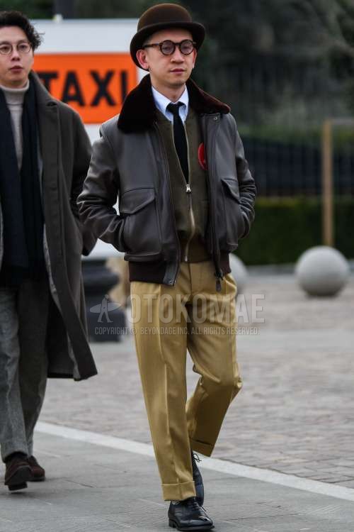 ブラウン無地のハット、ブラウン無地のメガネ、黒無地のレザージャケット(ライダース以外)、黒無地のミリタリージャケット(MA-1、M-65以外)、オリーブグリーン無地のカーディガン、白無地のシャツ、ベージュ無地のスラックス、グレー無地のソックス、黒ストレートチップの革靴、黒無地のニットタイを合わせた秋冬のメンズコーデ・着こなし。