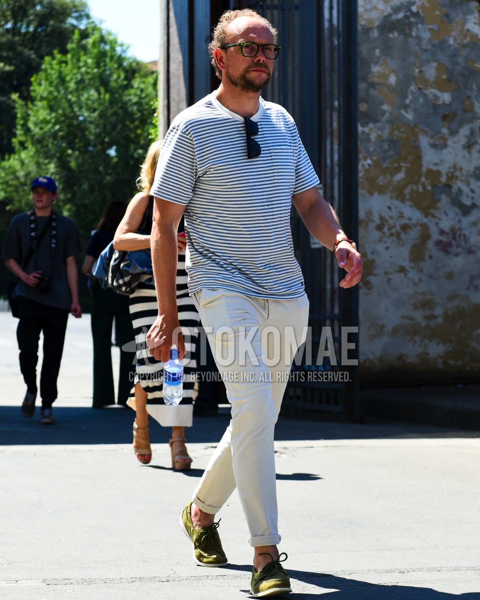 Men's spring summer outfit with green plain glasses, navy white horizontal stripes t-shirt, white plain cotton pants, olive green moccasins/deck shoes leather shoes.