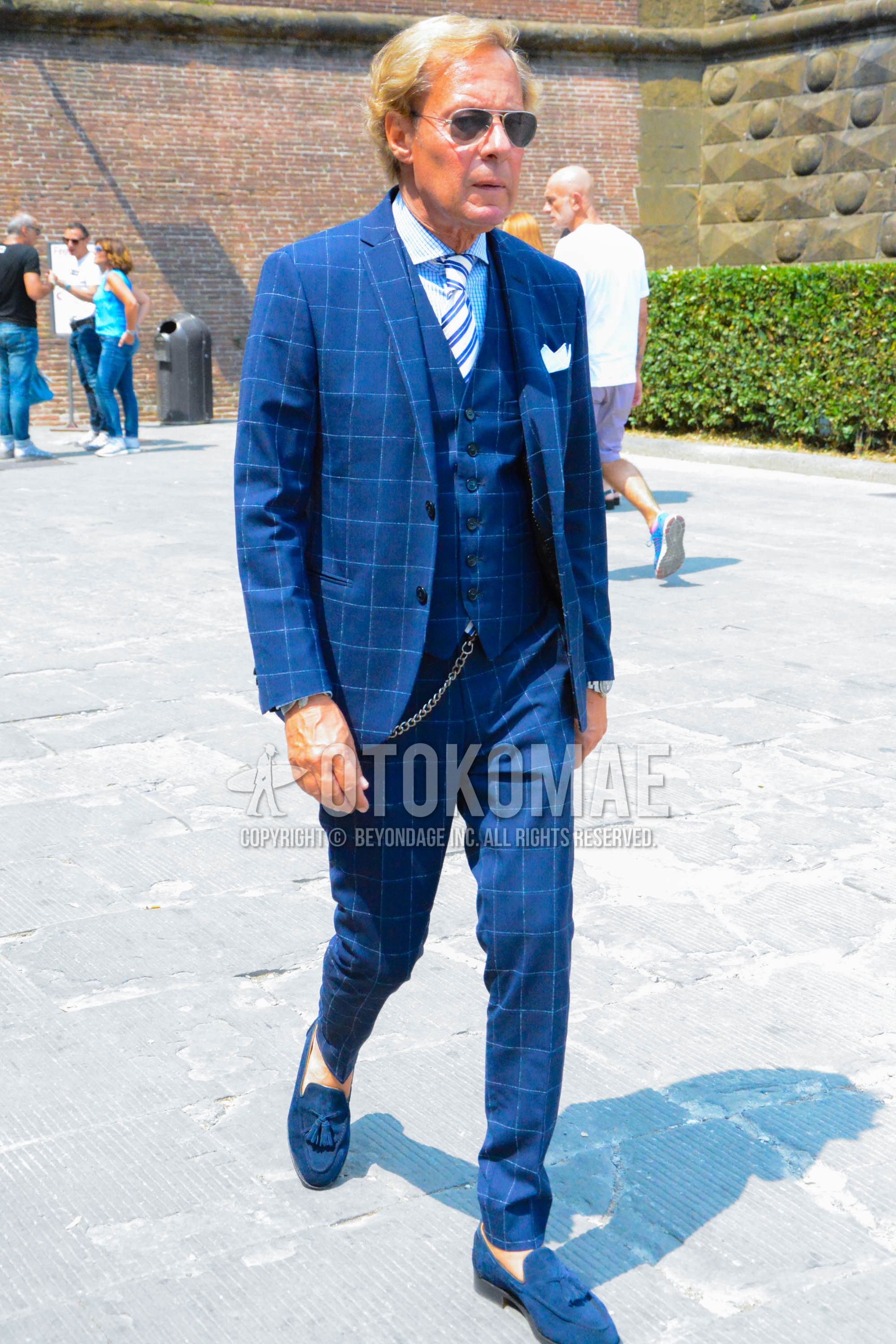 Men's spring autumn outfit with silver plain sunglasses, light blue check shirt, blue tassel loafers leather shoes, navy check three-piece suit, blue white regimental necktie.