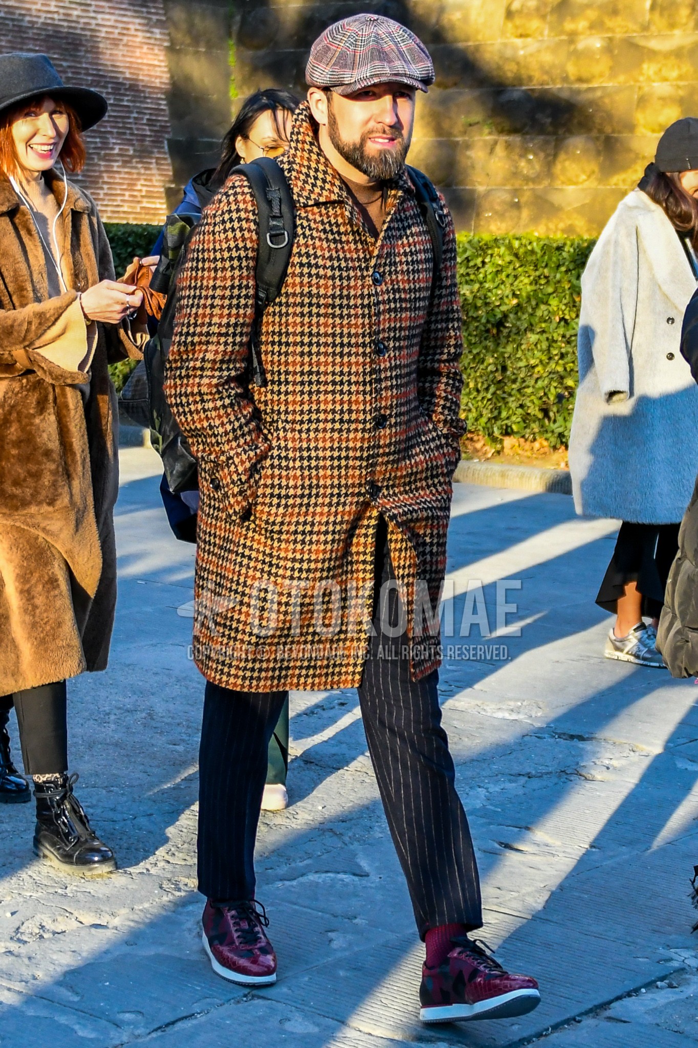 Men's winter outfit with brown check cap, brown check stenkarrer coat, brown plain turtleneck knit, navy plain slacks, red plain socks, red low-cut sneakers, black plain backpack.
