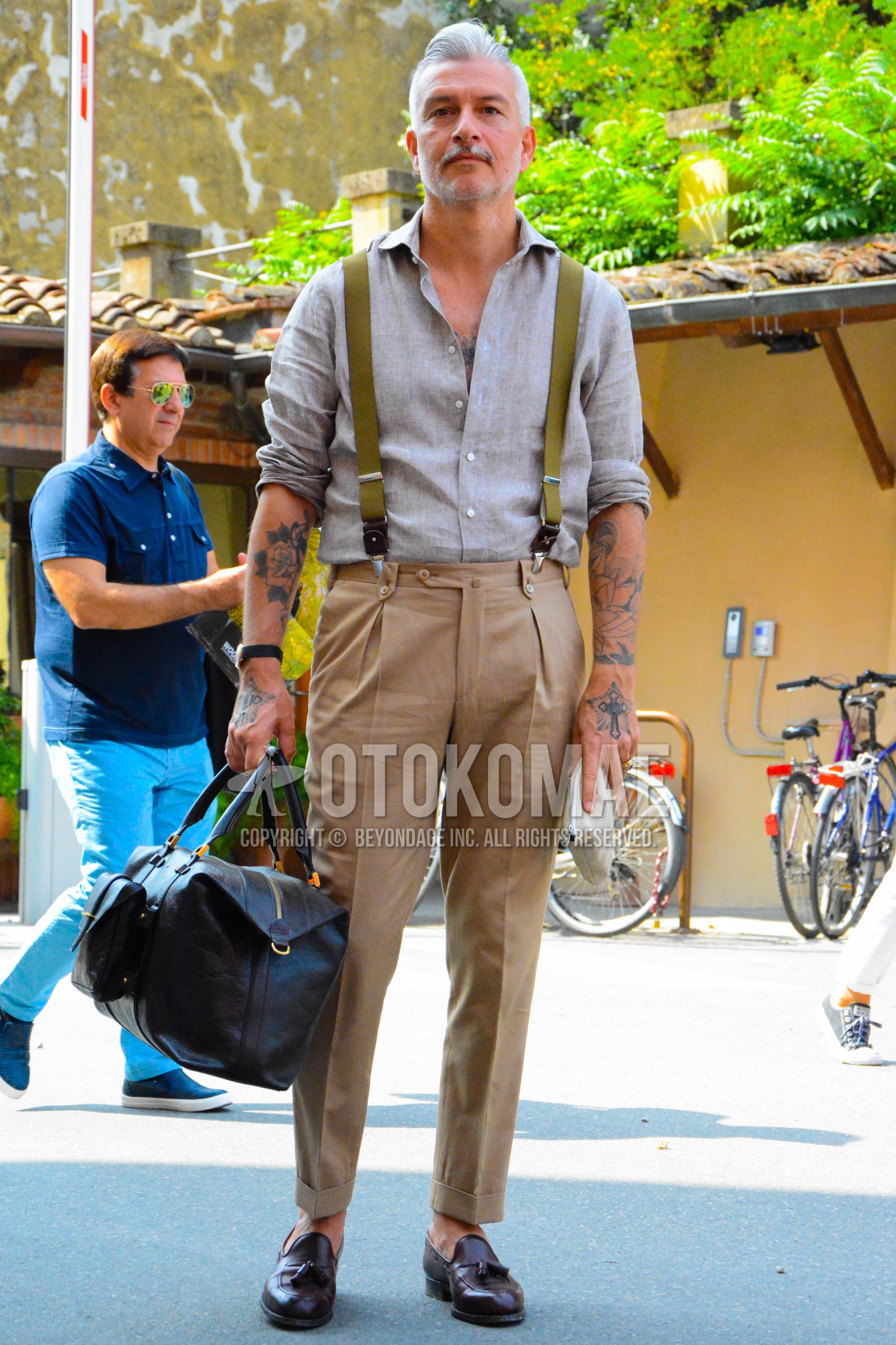 Men's spring summer outfit with gray plain shirt, olive green plain suspenders, beige plain slacks, beige plain pleated pants, beige plain ankle pants, brown tassel loafers leather shoes, brown plain boston bag.