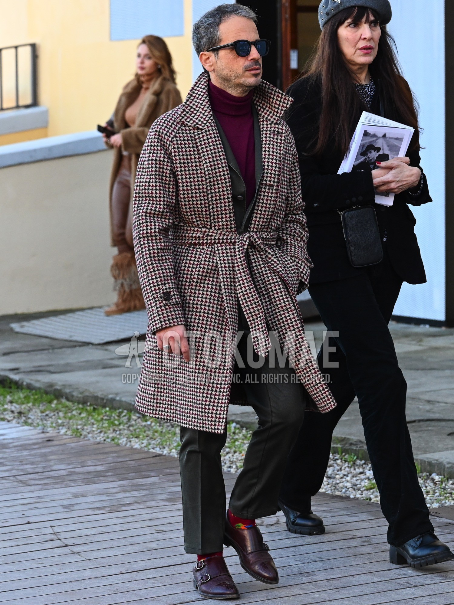 Men's autumn winter outfit with blue plain sunglasses, beige red black check belted coat, red plain turtleneck knit, red socks socks, brown monk shoes leather shoes, gray plain suit.