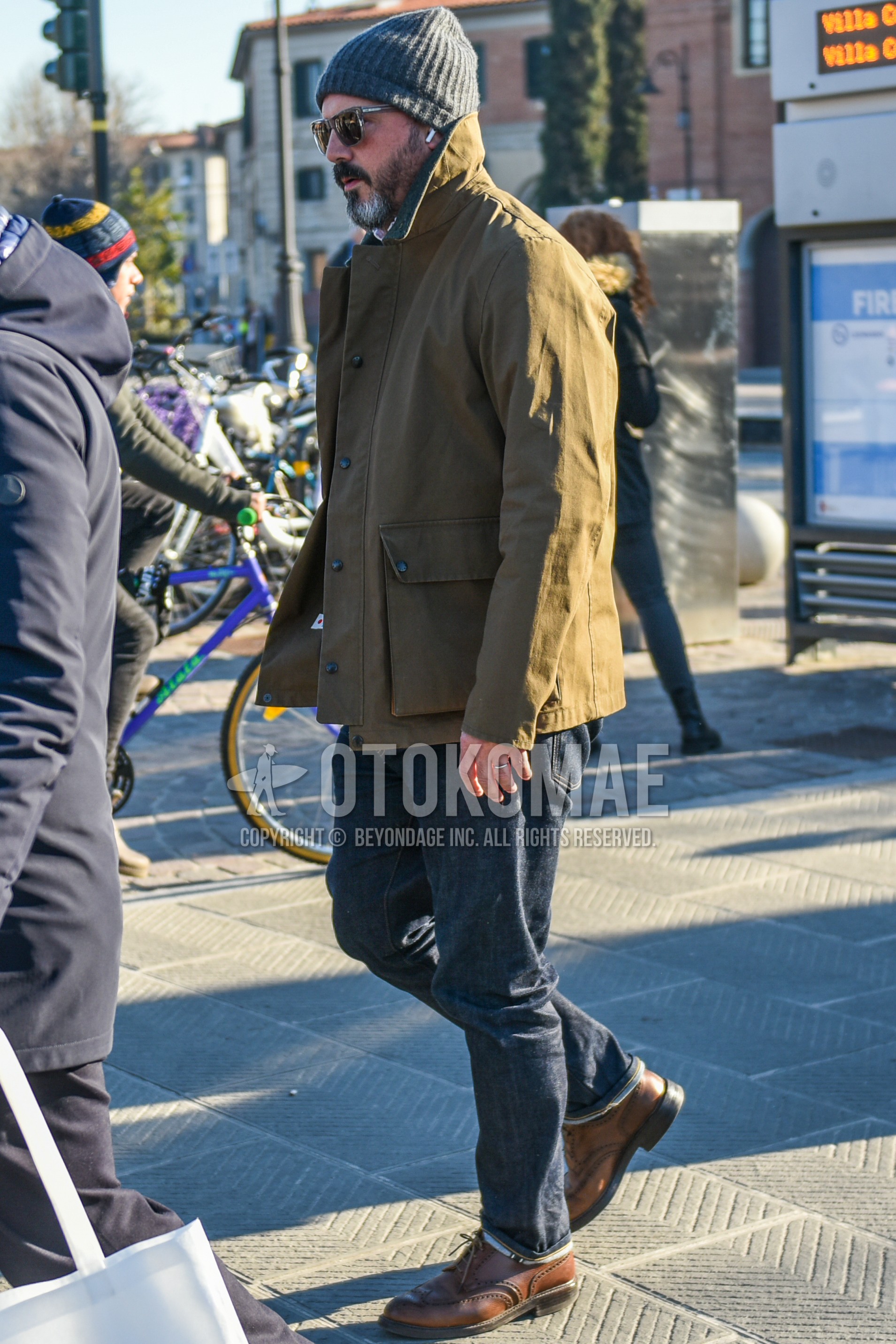 Men's autumn winter outfit with gray plain knit cap, gray plain sunglasses, beige plain coverall, navy plain denim/jeans, brown wing-tip shoes leather shoes.