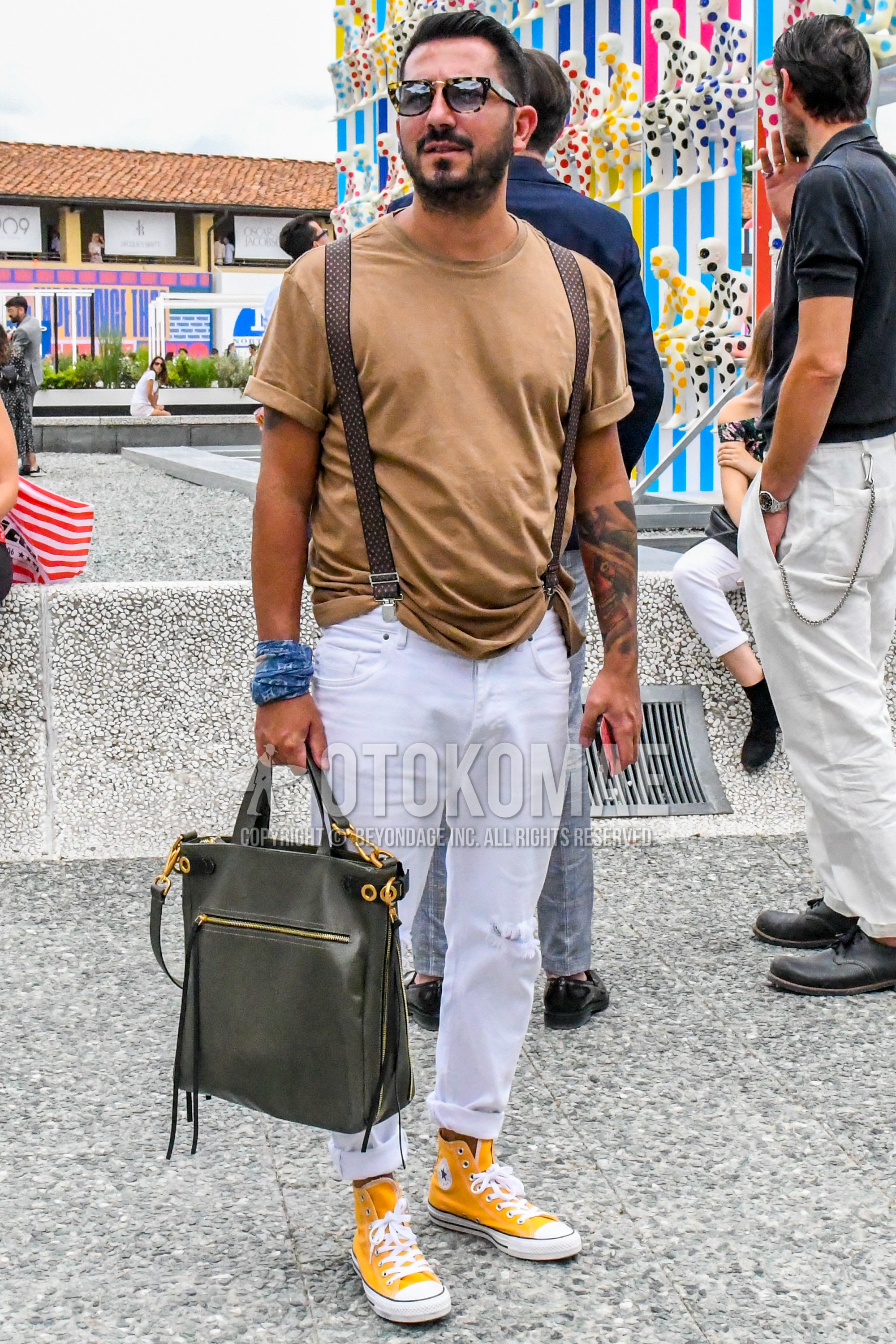 Men's spring summer outfit with beige tortoiseshell sunglasses, brown plain t-shirt, brown belt suspenders, white plain damaged jeans, yellow high-cut sneakers, gray plain briefcase/handbag.