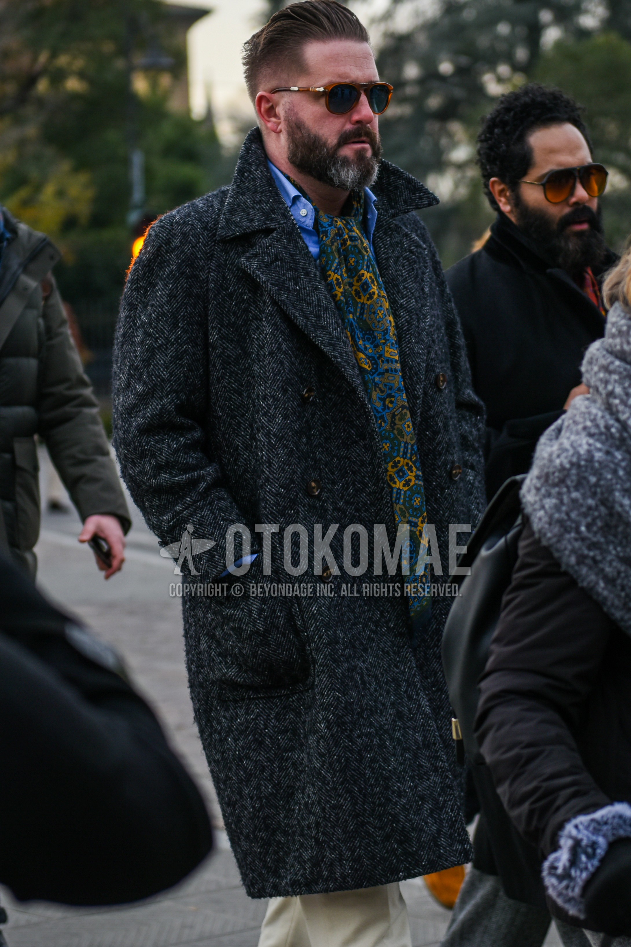 Men's autumn winter outfit with brown tortoiseshell sunglasses, multi-color scarf scarf, gray herringbone ulster coat, blue plain shirt, beige plain chinos.