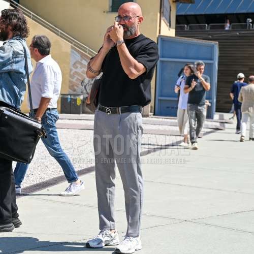 ティアドロップの黒無地のサングラス、黒無地のTシャツ、黒無地のレザーベルト、グレー無地のスラックス、ニューバランスの白ローカットのスニーカー、レザーのブラウンバッグのトートバッグを合わせた夏春のメンズコーデ・着こなし。