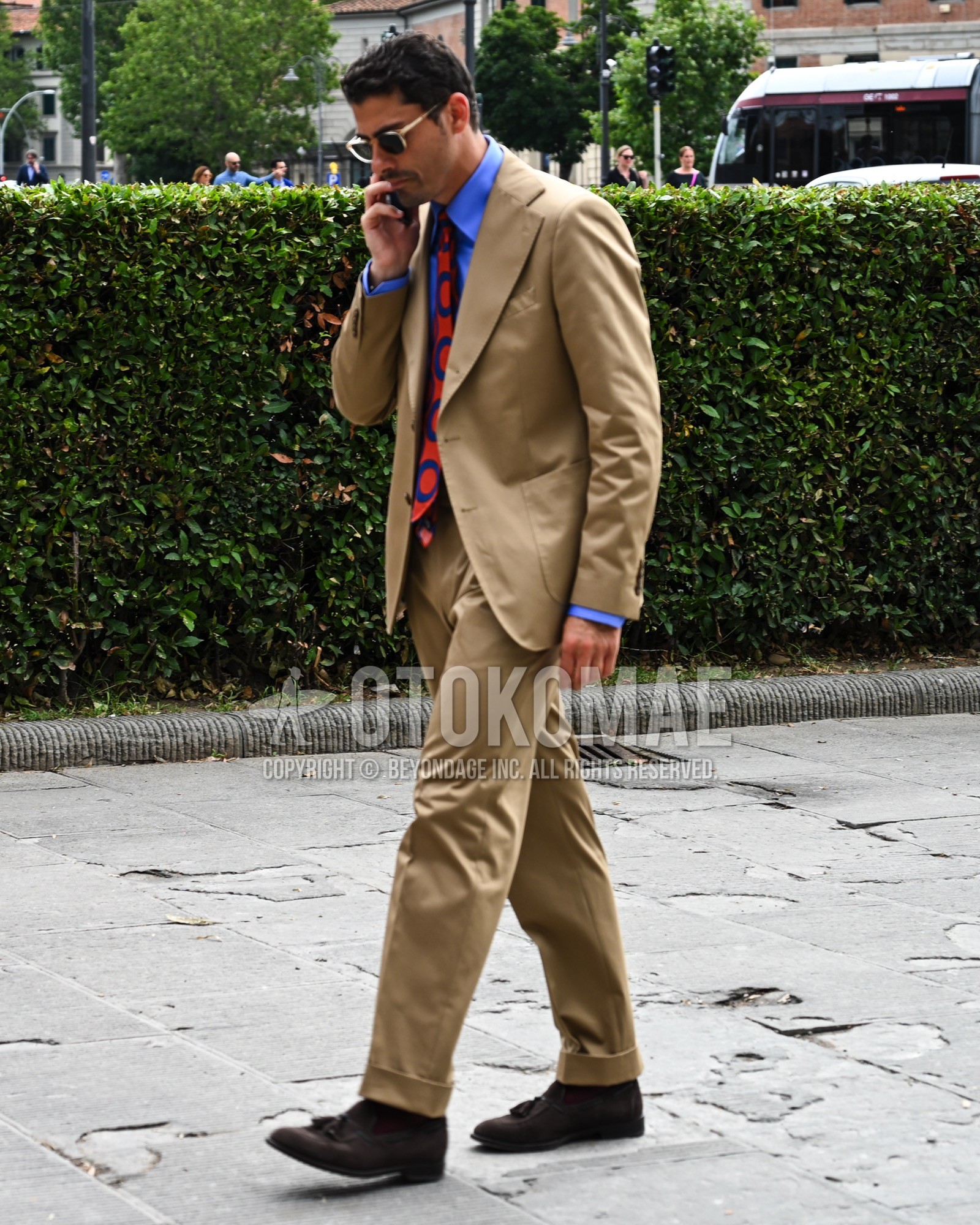 Men's spring summer autumn outfit with black plain sunglasses, blue plain shirt, brown plain socks, brown tassel loafers leather shoes, beige plain suit, orange necktie necktie.