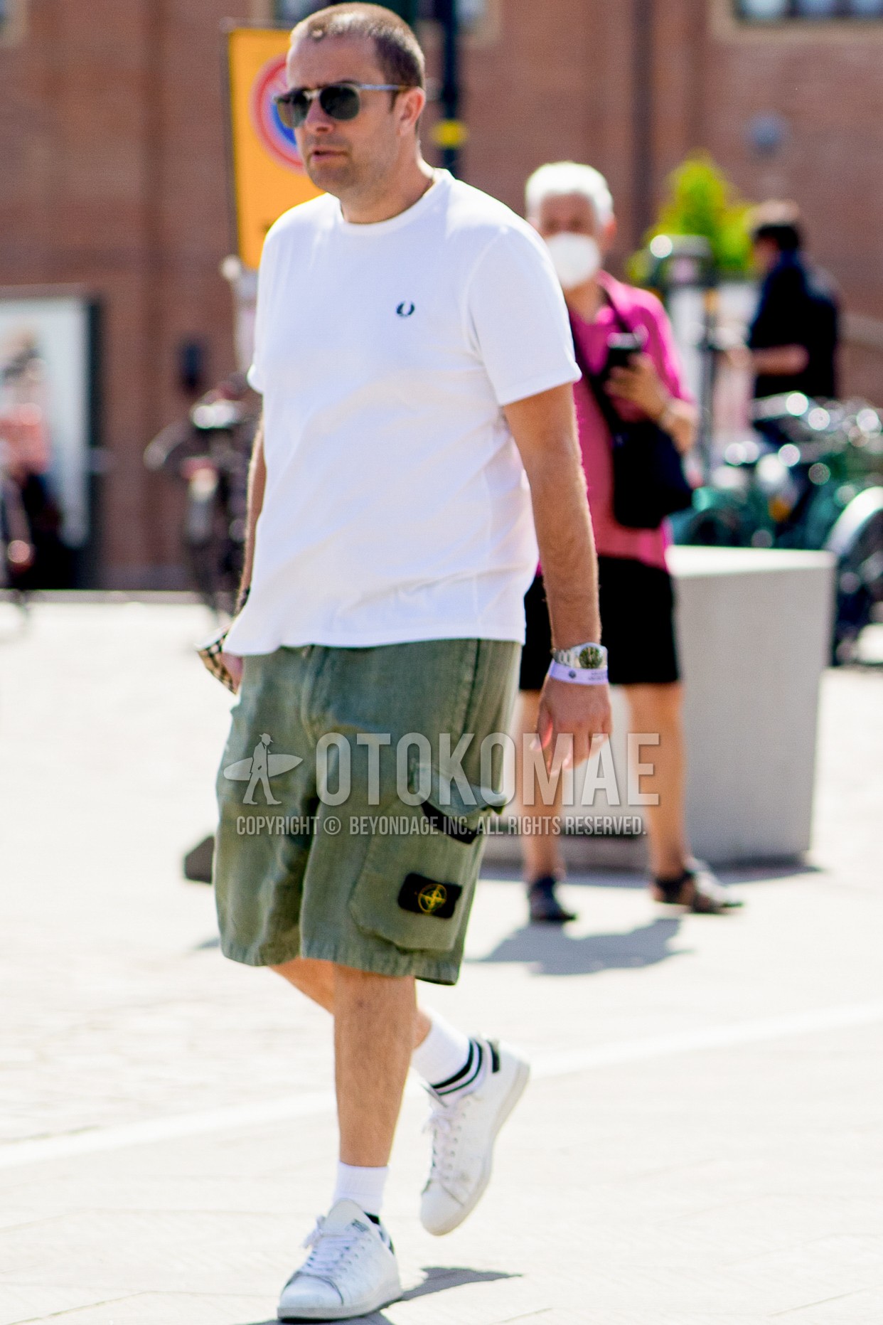 Men's spring summer outfit with silver plain sunglasses, white plain t-shirt, olive green plain short pants, white horizontal stripes socks, white sneakers.