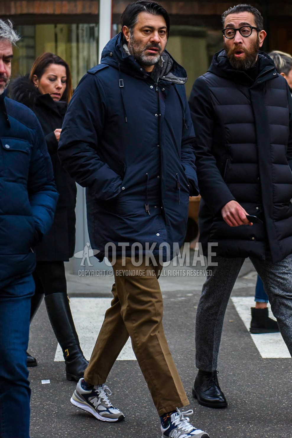 Men's winter outfit with navy plain hooded coat, beige plain chinos, navy socks socks, gray navy low-cut sneakers.