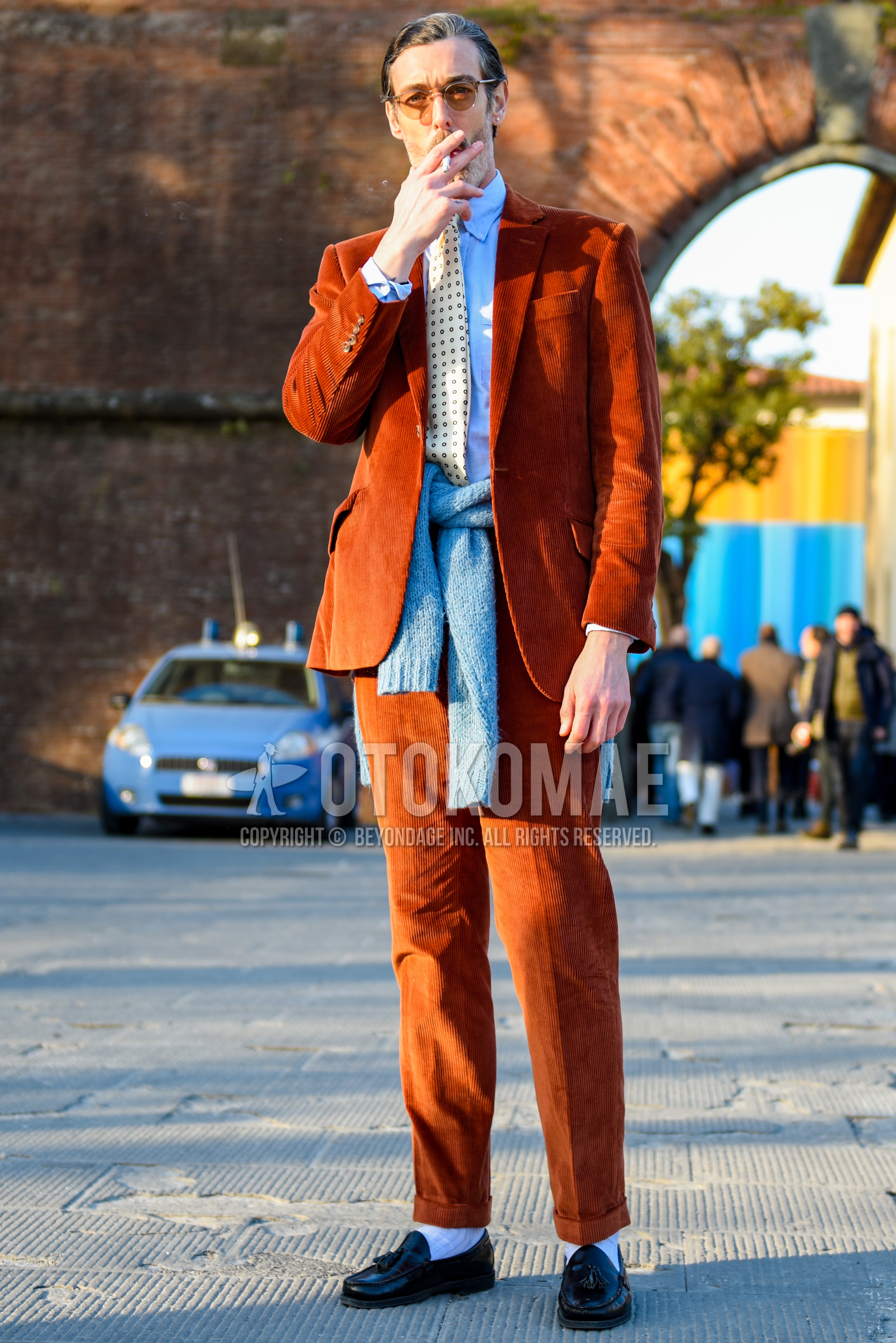 Men's spring autumn outfit with orange plain sunglasses, light blue plain shirt, gray plain sweater, white plain socks, black tassel loafers leather shoes, orange plain suit, beige necktie necktie.