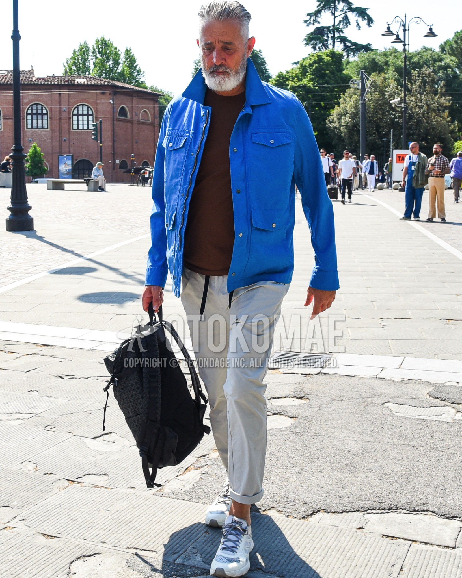 Men's spring summer outfit with blue plain field jacket/hunting jacket, brown plain t-shirt, gray plain cotton pants, white low-cut sneakers, black plain backpack.