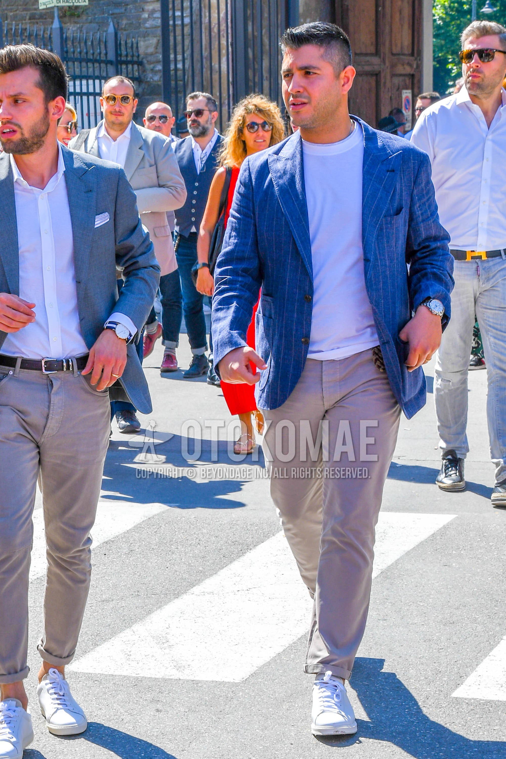 Men's spring summer autumn outfit with blue plain tailored jacket, white plain t-shirt, beige plain chinos, white low-cut sneakers.