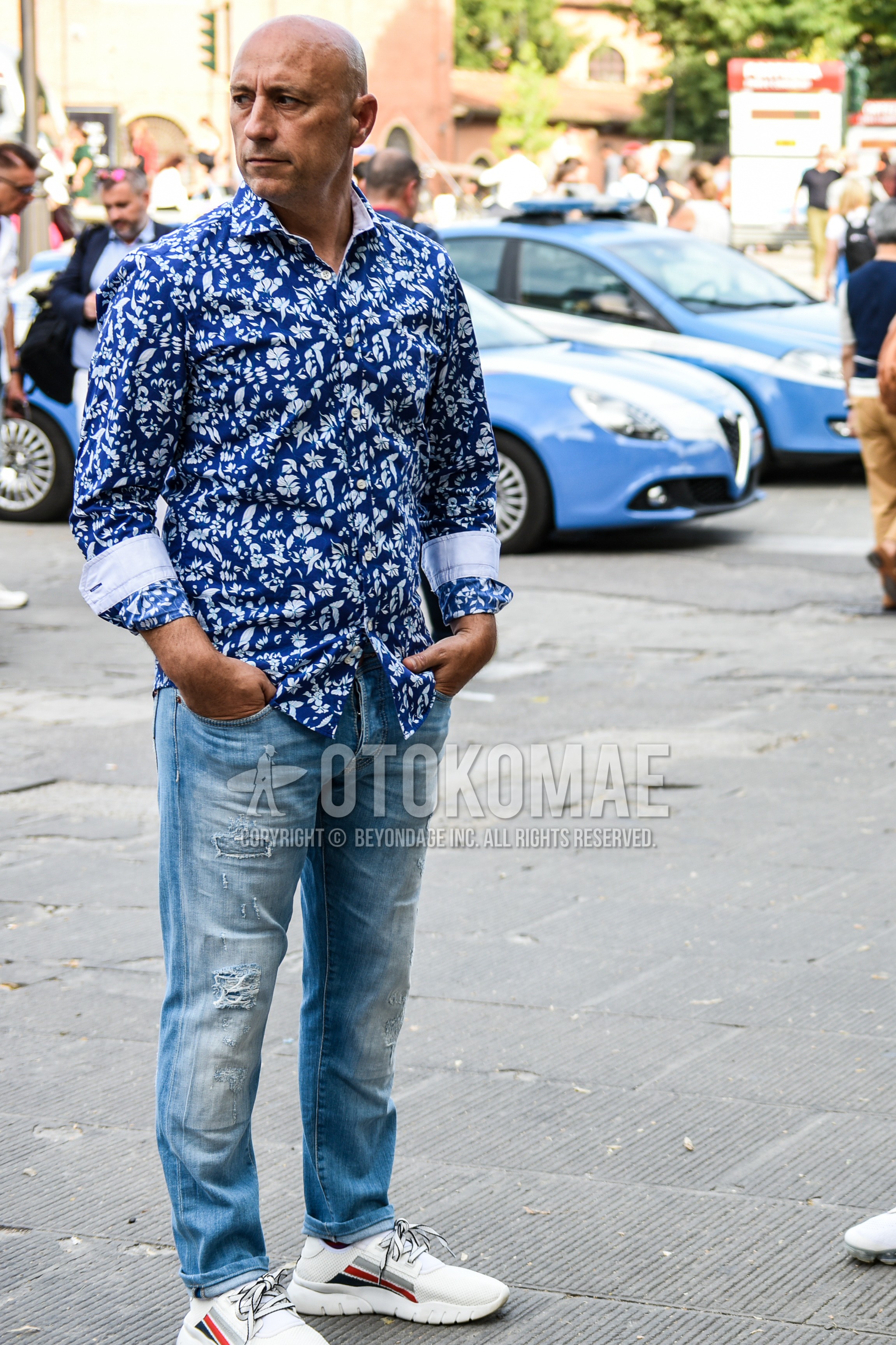 Men's spring autumn outfit with blue botanical shirt, blue plain damaged jeans, white low-cut sneakers.