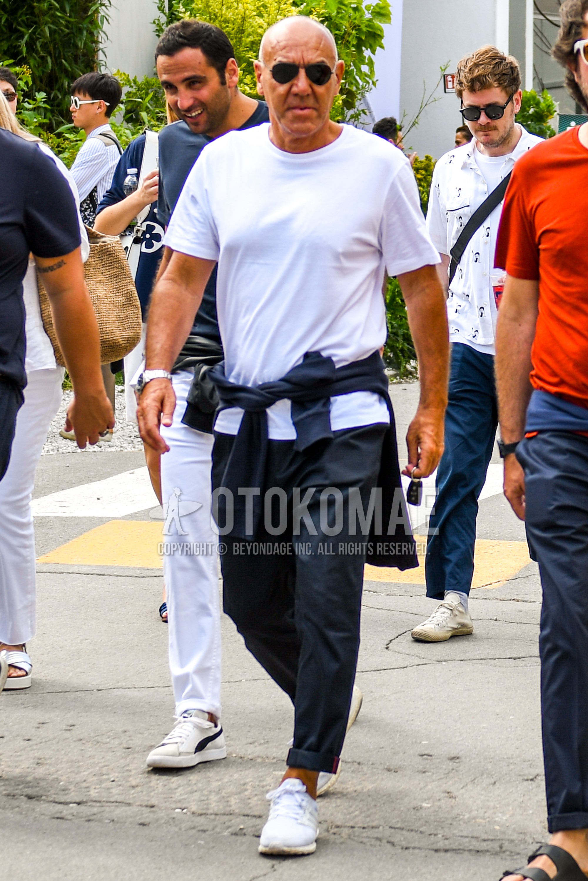 Men's spring summer outfit with plain sunglasses, white plain t-shirt, navy plain cotton pants, white low-cut sneakers.