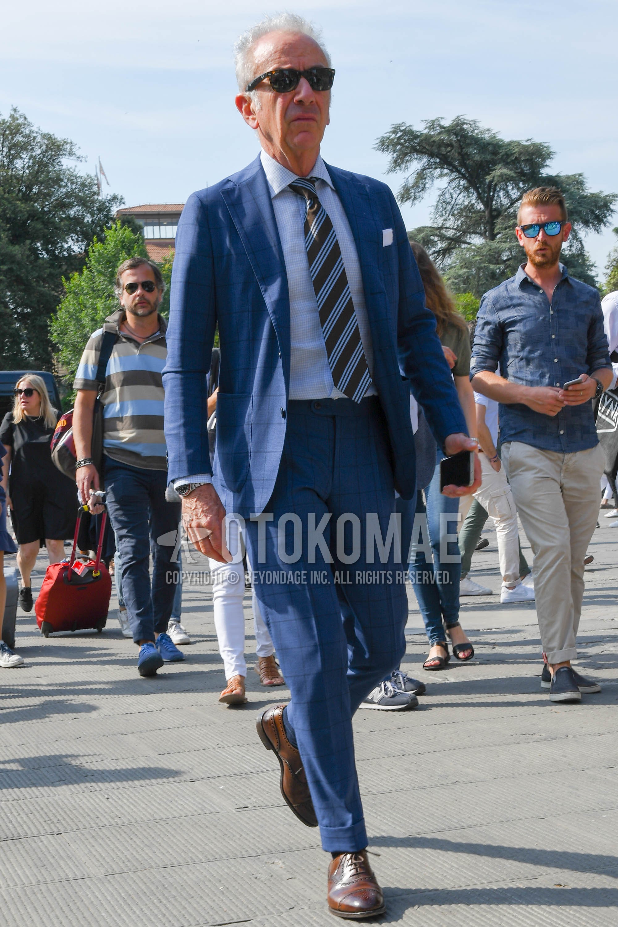 Men's spring autumn outfit with brown tortoiseshell sunglasses, white check shirt, brown wing-tip shoes leather shoes, blue check suit, brown regimental necktie.