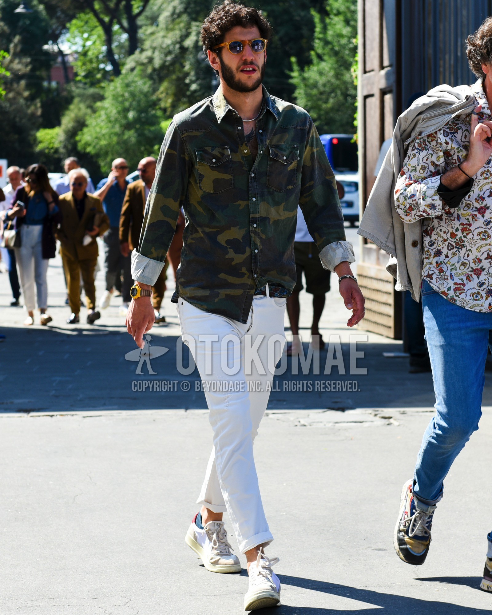 Men's spring summer outfit with yellow tortoiseshell sunglasses, olive green camouflage denim shirt/chambray shirt, black belt leather belt, white plain cotton pants, white plain cropped pants, white beige low-cut sneakers.