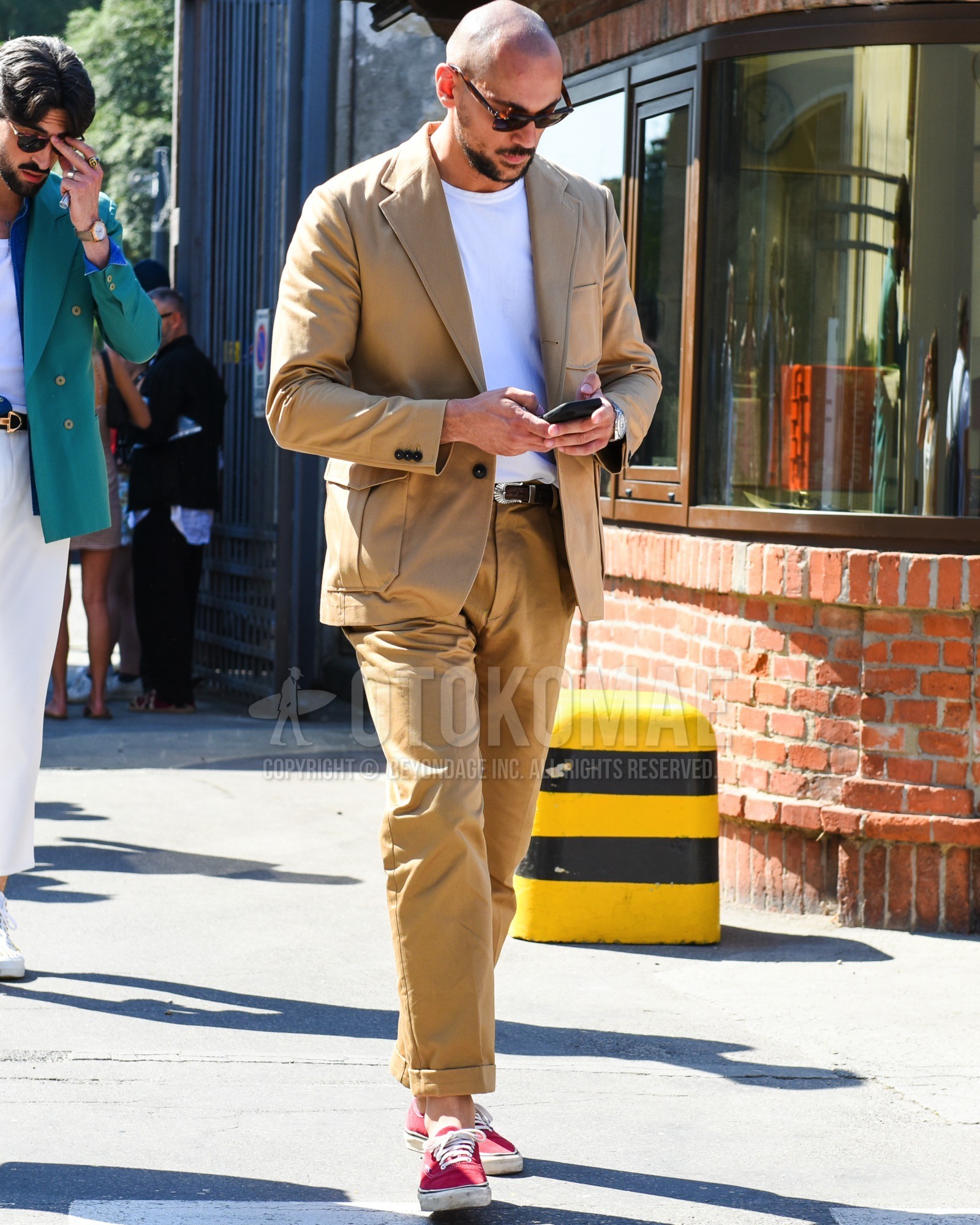 Men's spring summer outfit with brown tortoiseshell sunglasses, beige plain tailored jacket, white plain t-shirt, brown plain leather belt, beige plain slacks, beige plain ankle pants, pink low-cut sneakers.