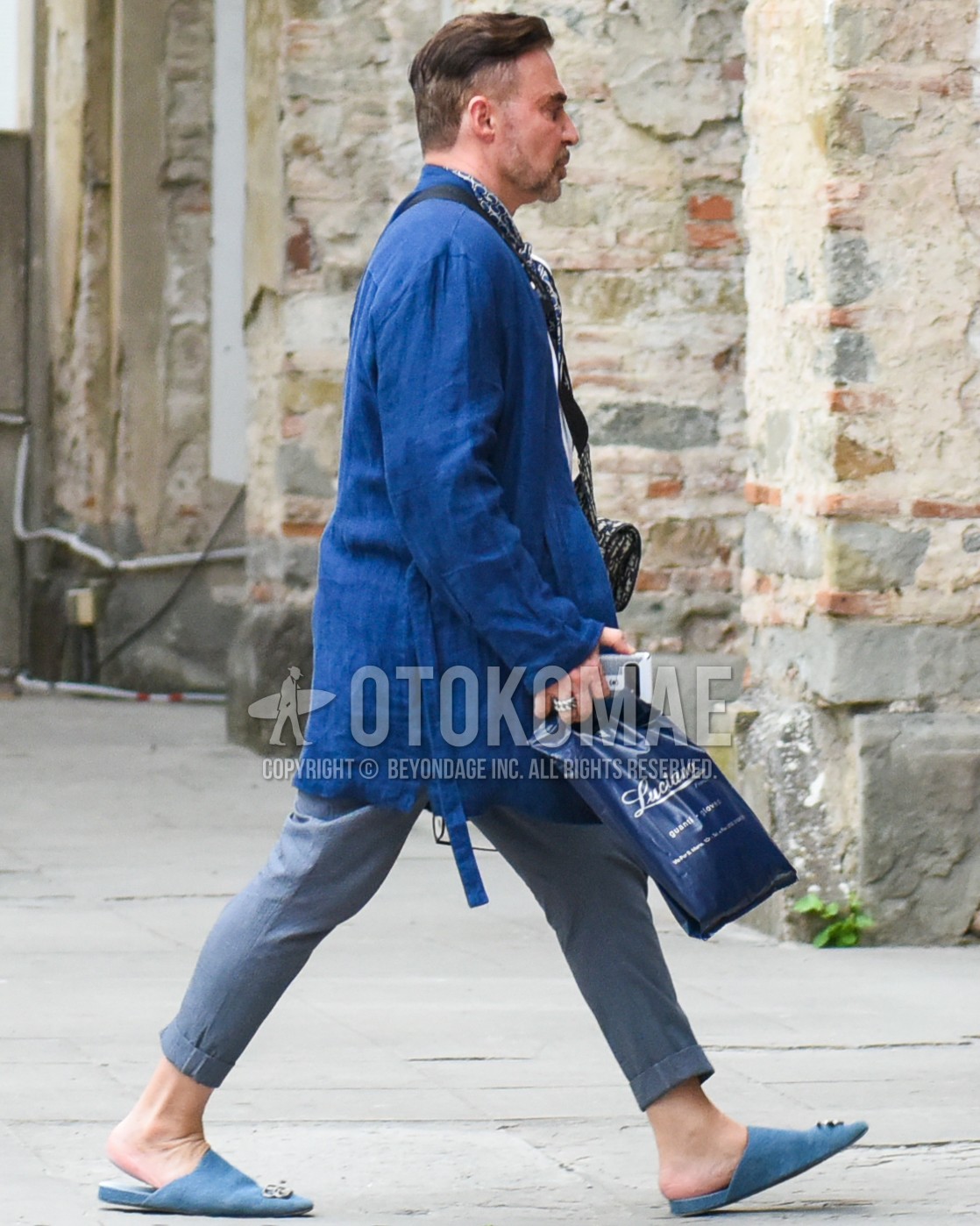 Men's spring summer outfit with blue plain belted coat, gray plain slacks, gray plain cropped pants, blue leather sandals.
