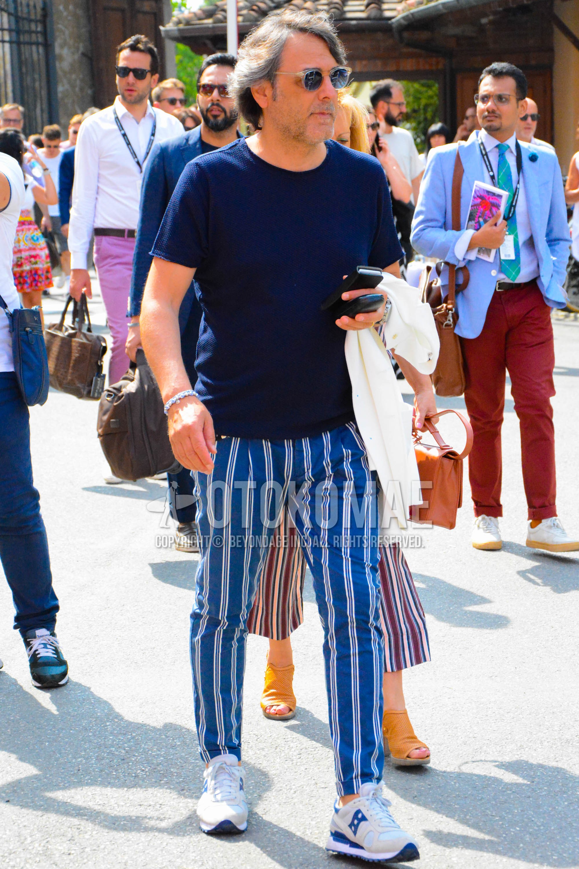 Men's spring summer outfit with clear plain sunglasses, navy plain t-shirt, blue stripes cotton pants, white low-cut sneakers.