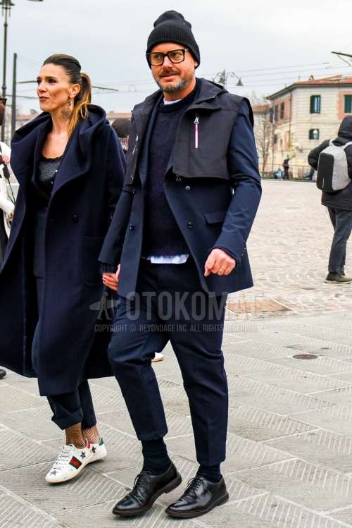 黒無地のニットキャップ、黒無地のメガネ、ダークグレー無地のアウター、白無地のTシャツ、ダークグレー無地のセーター、ネイビー無地のソックス、黒プレーントゥの革靴、ネイビー無地のスーツを合わせた秋冬のメンズコーデ・着こなし。