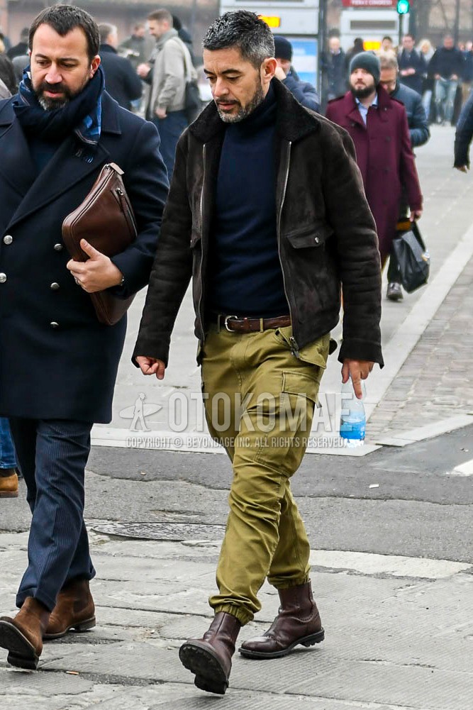 Men's winter outfit with brown plain leather jacket, brown plain military jacket, navy plain turtleneck knit, brown plain leather belt, olive green plain cargo pants, brown side-gore boots.