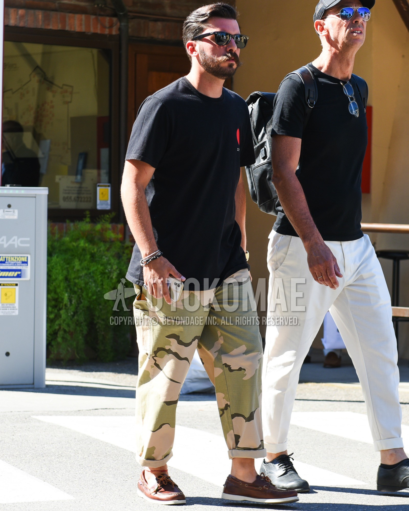 Men's spring summer outfit with black plain sunglasses, black plain t-shirt, green camouflage chinos, brown moccasins/deck shoes leather shoes.