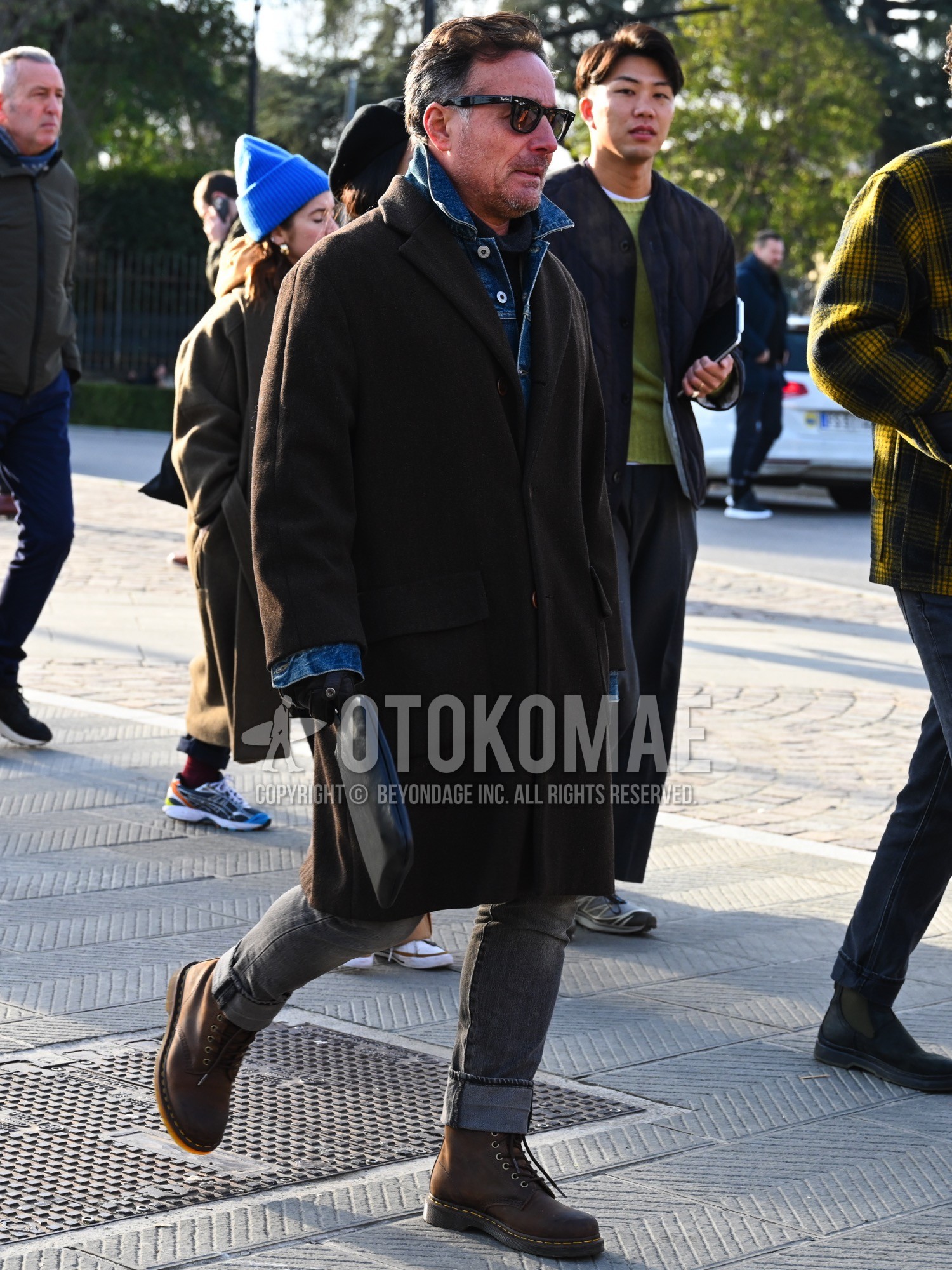 Men's autumn winter outfit with black plain sunglasses, blue plain denim jacket, brown plain chester coat, dark gray plain turtleneck knit, gray plain denim/jeans, brown work boots.
