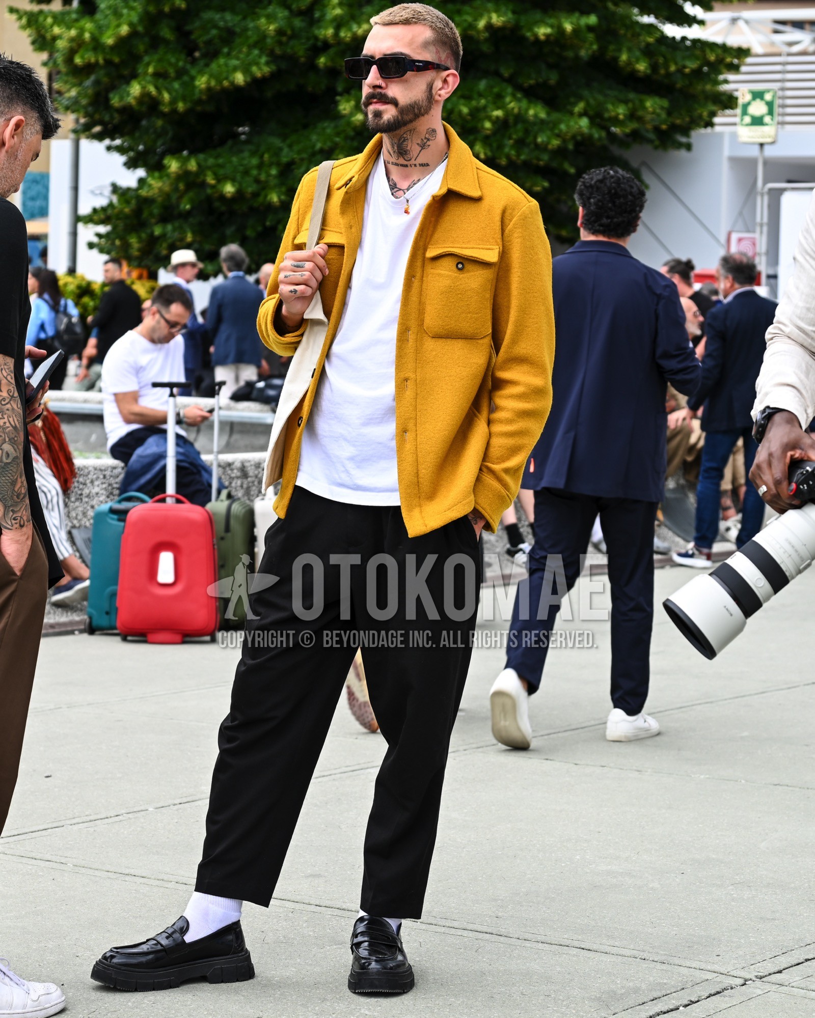 Men's spring summer autumn outfit with black tortoiseshell sunglasses, yellow plain outerwear, white plain t-shirt, black plain chinos, white plain socks, black coin loafers leather shoes, beige plain tote bag.