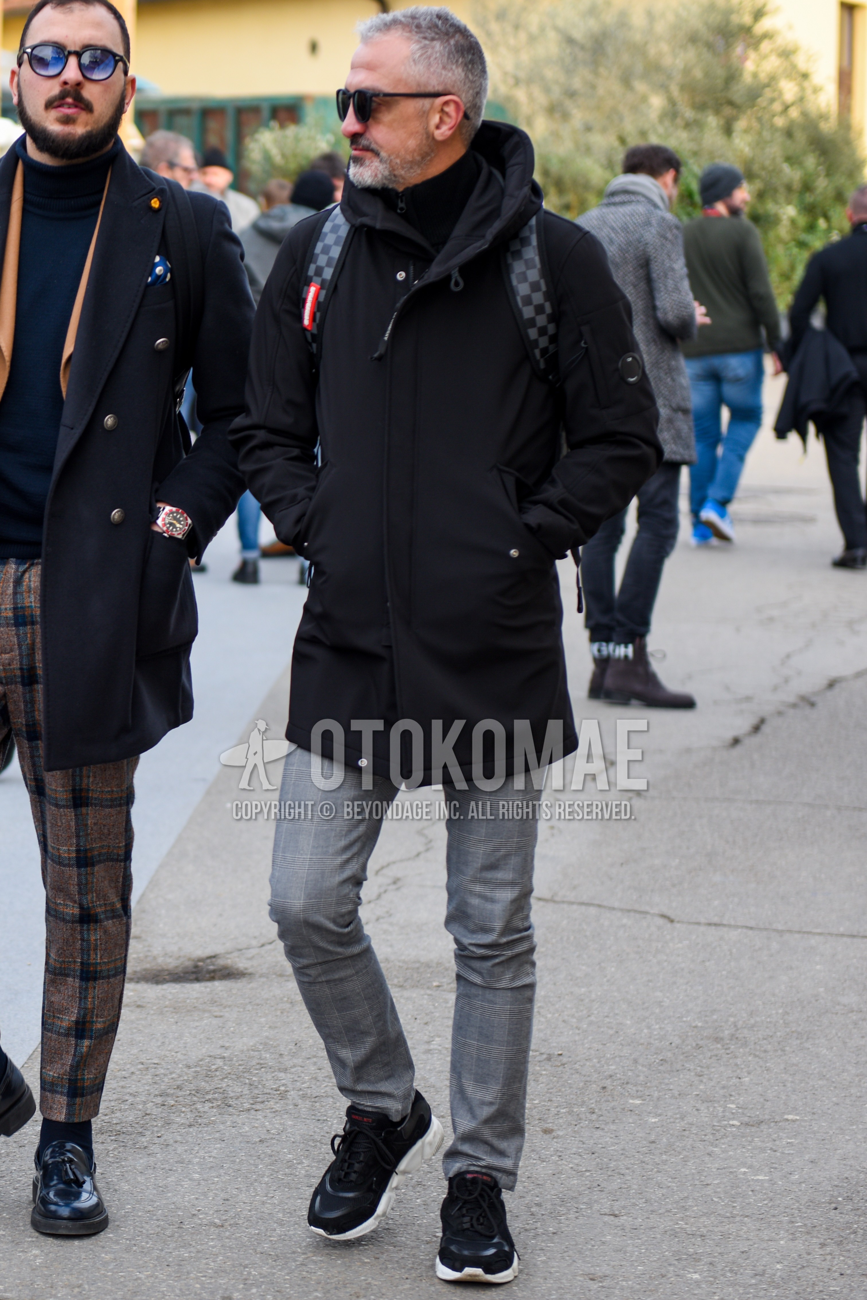 Men's autumn winter outfit with black plain sunglasses, black plain hooded coat, gray check slacks, black low-cut sneakers.
