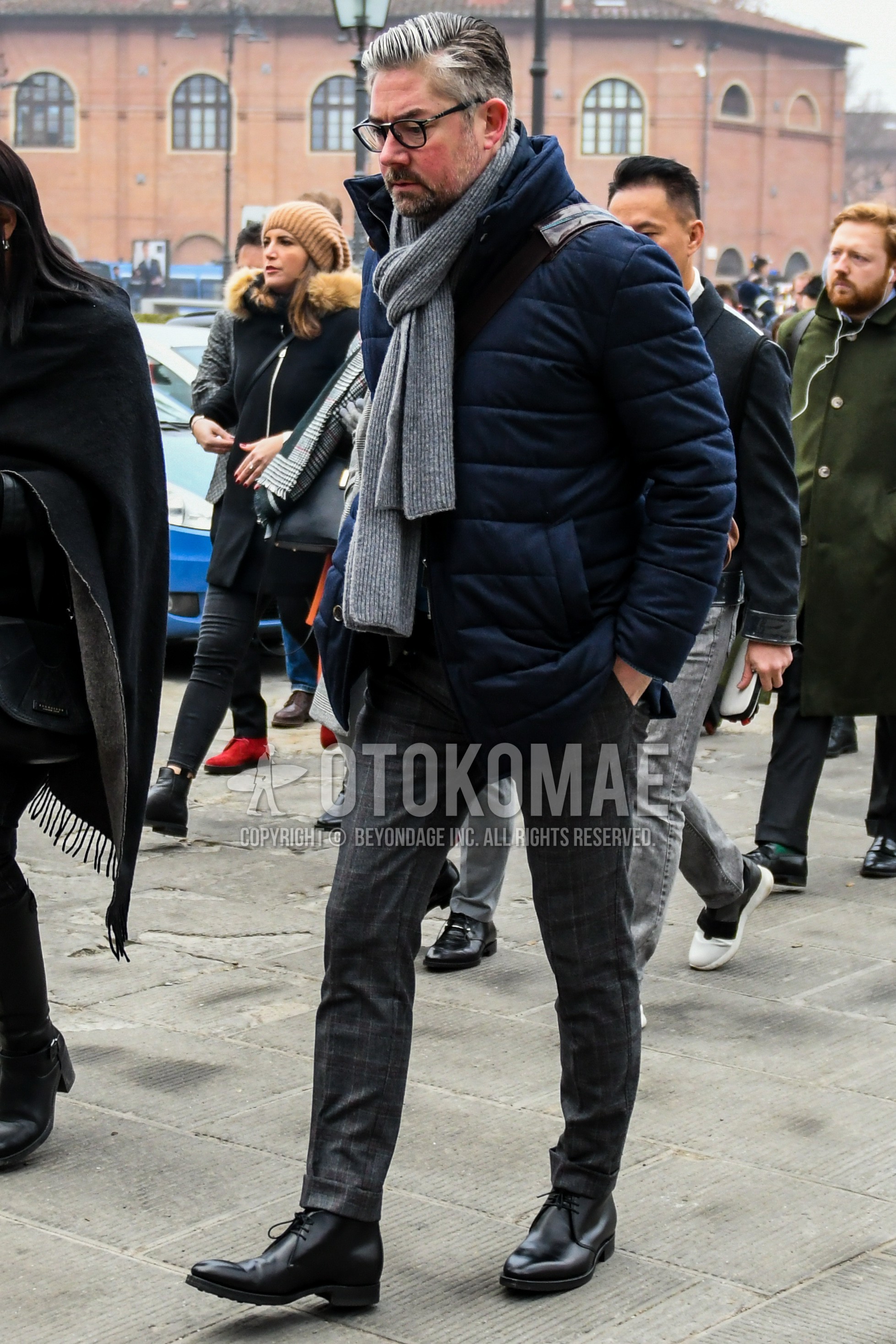 Men's winter outfit with plain glasses, gray plain scarf, navy plain down jacket, gray check slacks, black chukka boots.