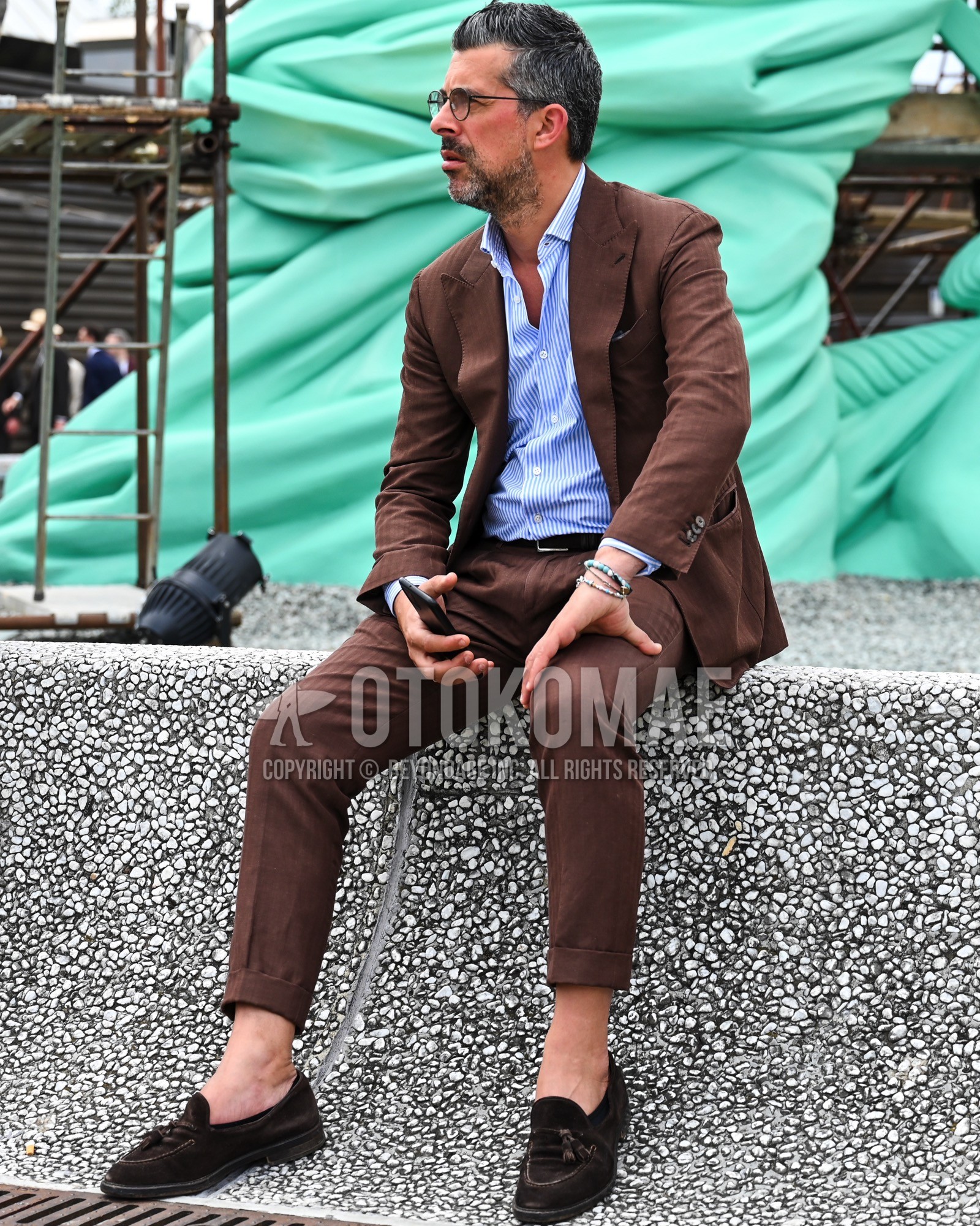 Men's spring summer autumn outfit with clear plain glasses, light blue stripes shirt, brown plain leather belt, brown tassel loafers leather shoes, brown suede shoes leather shoes, brown plain suit.