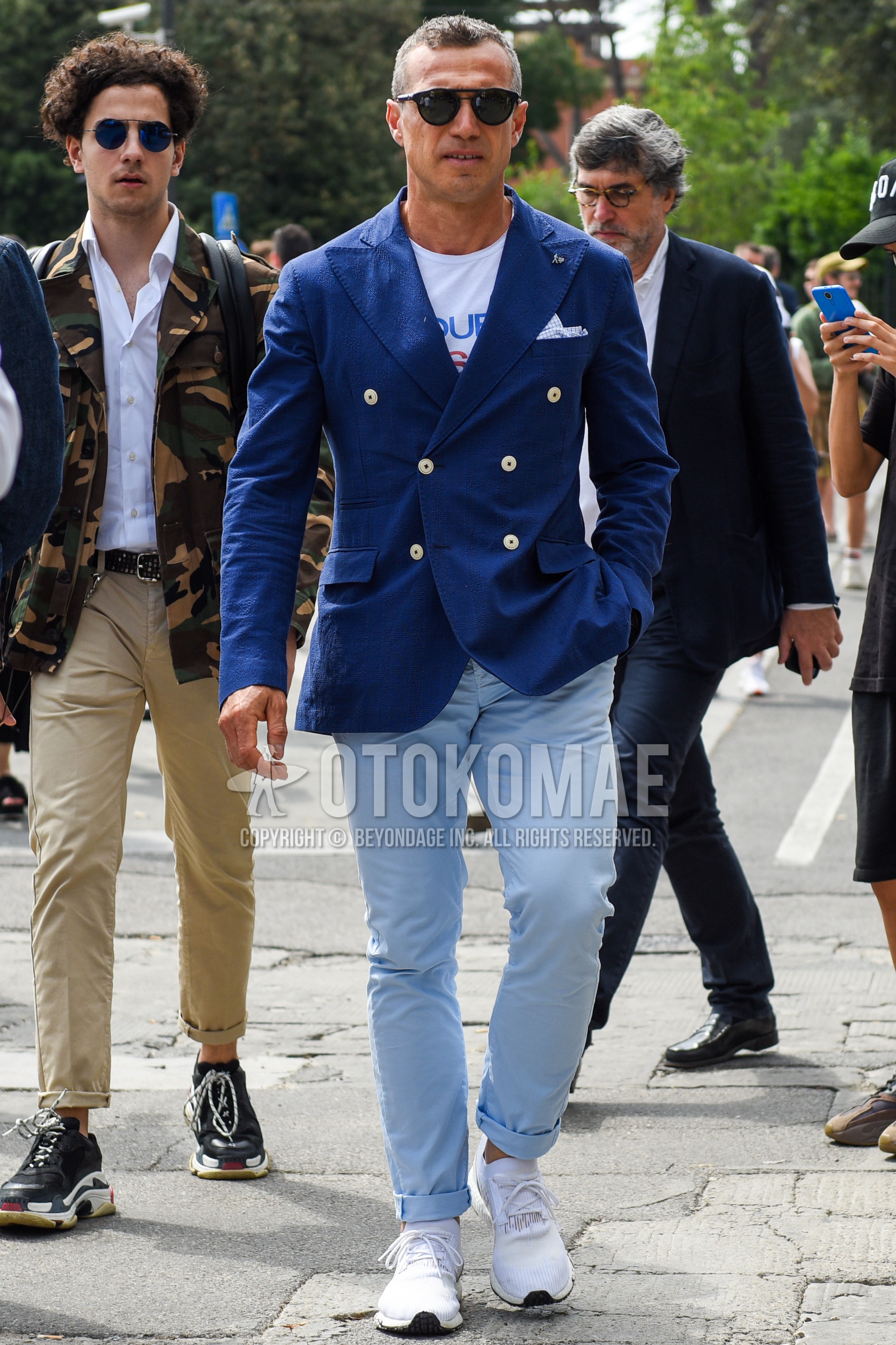 Men's spring summer autumn outfit with navy plain tailored jacket, white graphic t-shirt, light blue plain cotton pants, white low-cut sneakers.