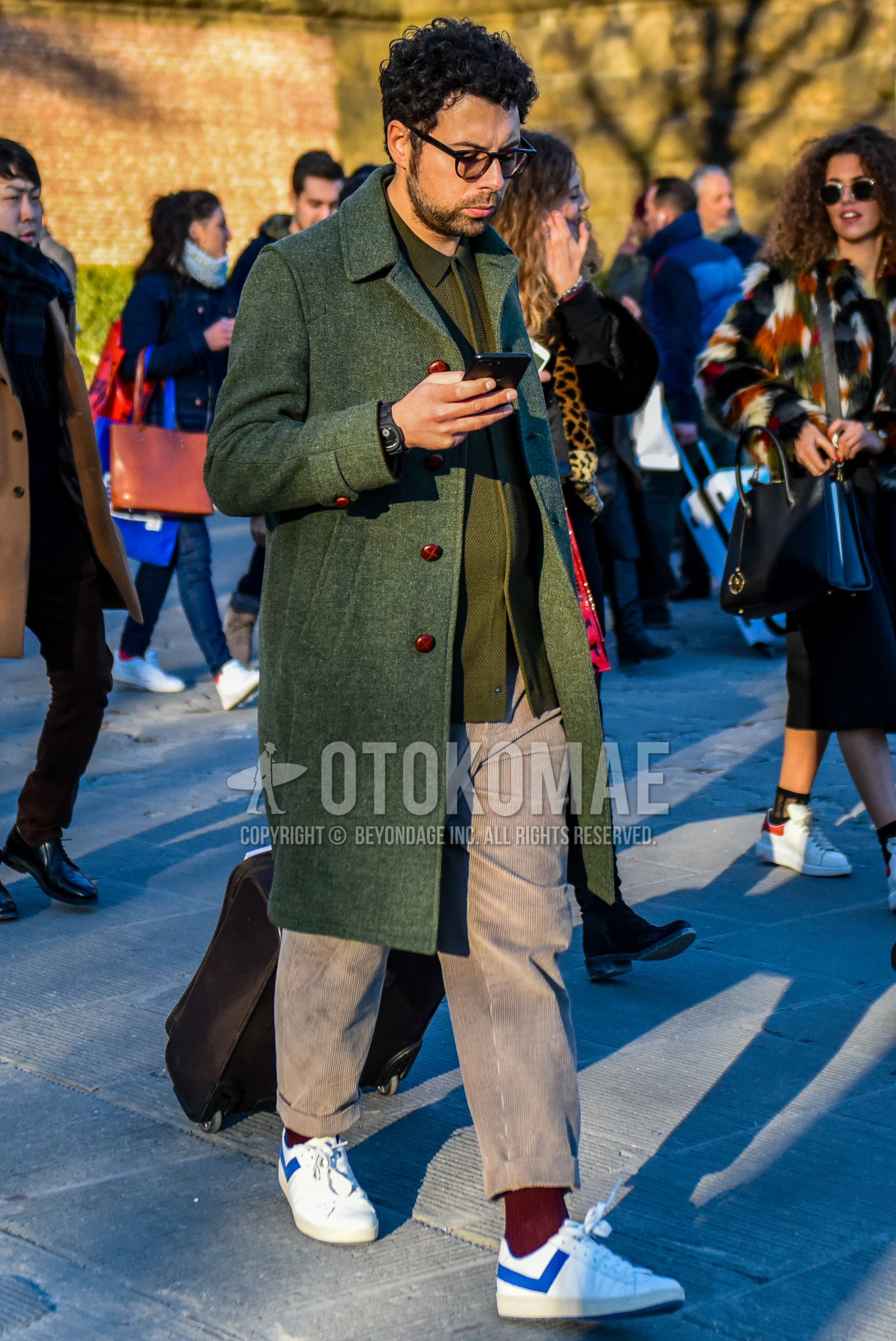 Men's autumn winter outfit with black plain glasses, green plain stenkarrer coat, olive green plain shirt jacket, beige plain winter pants (corduroy,velour), red plain socks, white low-cut sneakers.
