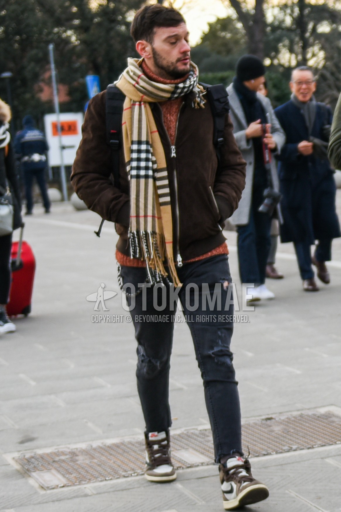 Men's autumn winter outfit with beige check scarf, brown plain leather jacket, brown tops/innerwear turtleneck knit, gray plain damaged jeans, brown high-cut sneakers, black plain backpack.