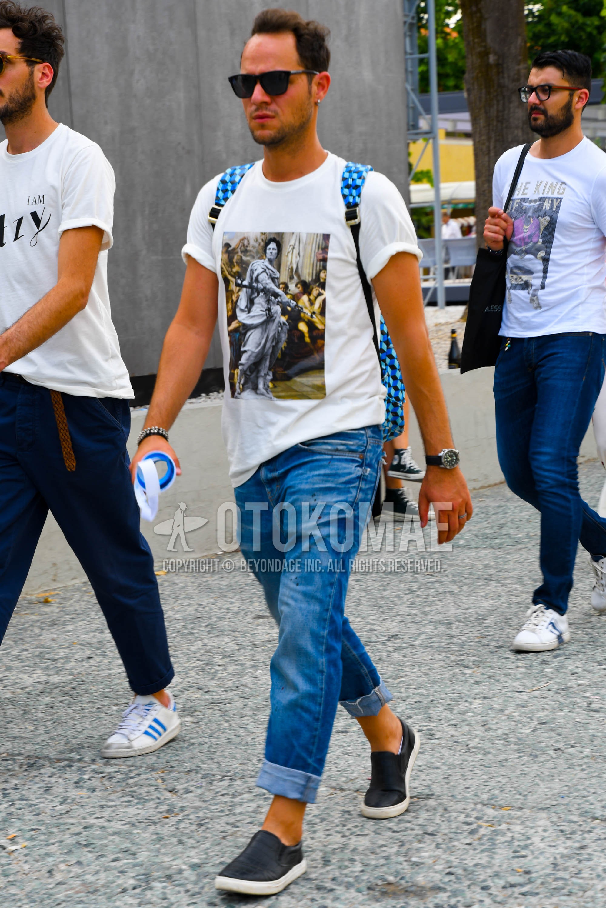 Men's summer outfit with plain sunglasses, white graphic t-shirt, blue plain denim/jeans, black slip-on sneakers.