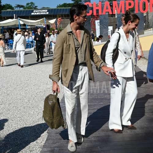 黒無地のサングラス、オリーブグリーン無地のサファリジャケット、オリーブグリーン無地のシャツ、白無地のスラックス、白無地のベルトレスパンツ、白無地のアンクルパンツ、白タッセルローファーの革靴、レザーのグリーン無地のバックパックを合わせた春夏のメンズコーデ・着こなし。