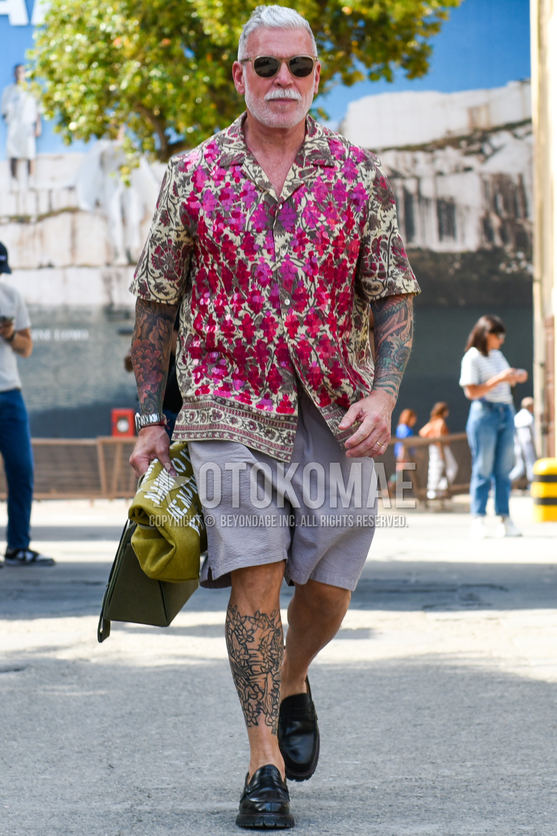 Men's summer outfit with clear plain sunglasses, multi-color tops/innerwear shirt, gray plain short pants, black coin loafers leather shoes, olive green graphic clutch bag/second bag/drawstring bag.