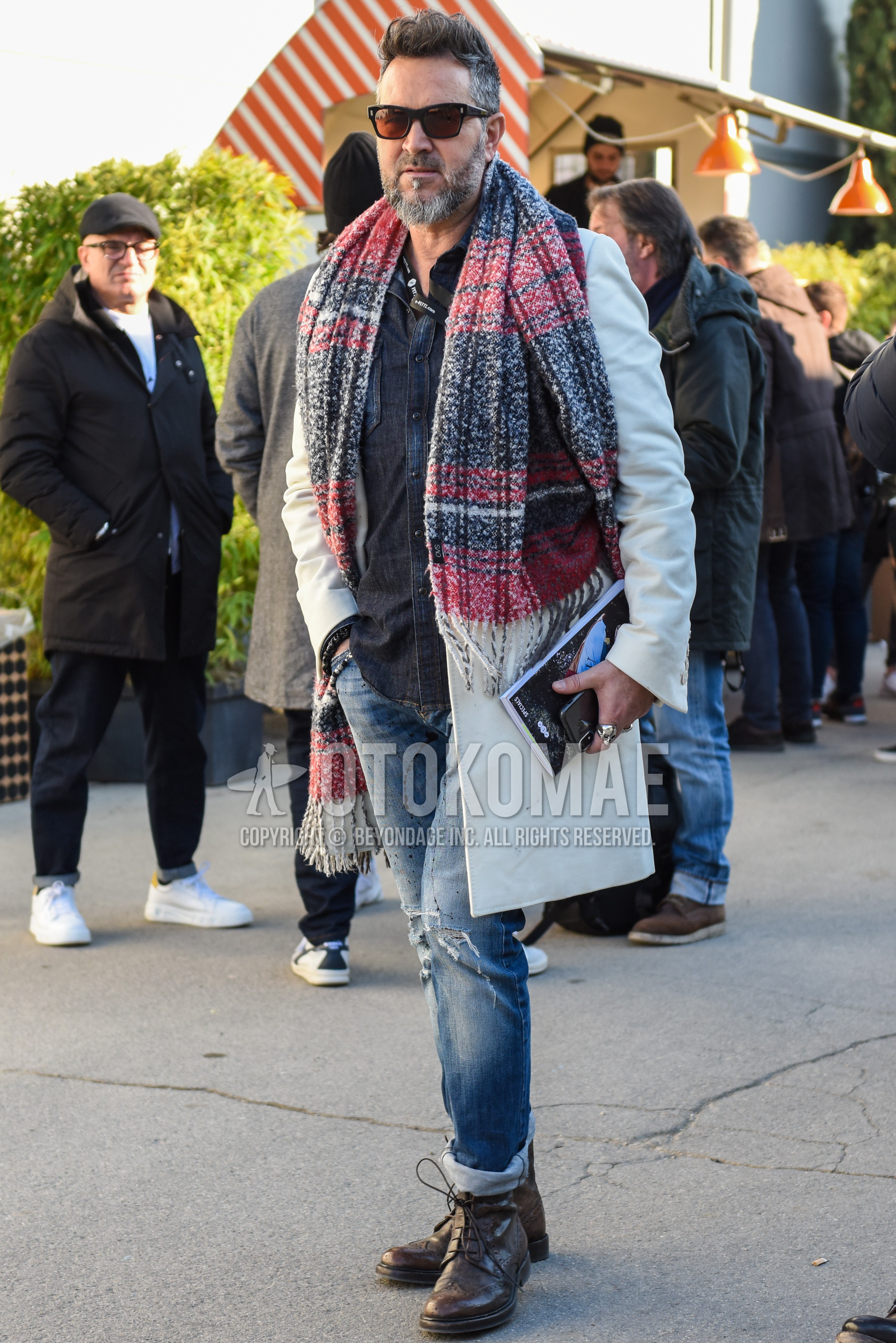 Men's autumn winter outfit with black plain sunglasses, multi-color scarf scarf, white plain chester coat, dark gray plain denim shirt/chambray shirt, blue plain damaged jeans, brown  boots.