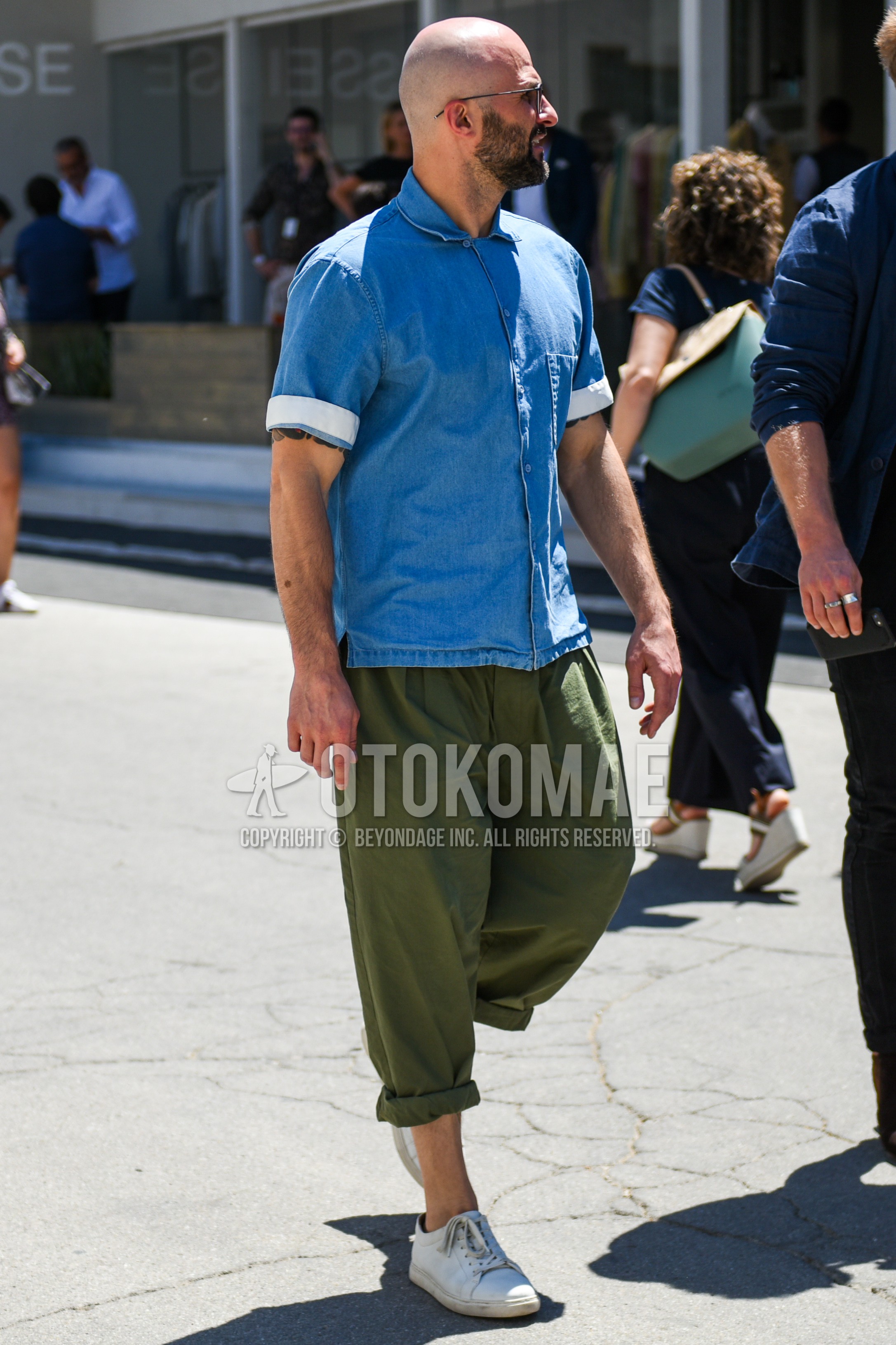 Men's summer outfit with blue plain denim shirt/chambray shirt, green plain wide pants, white low-cut sneakers.