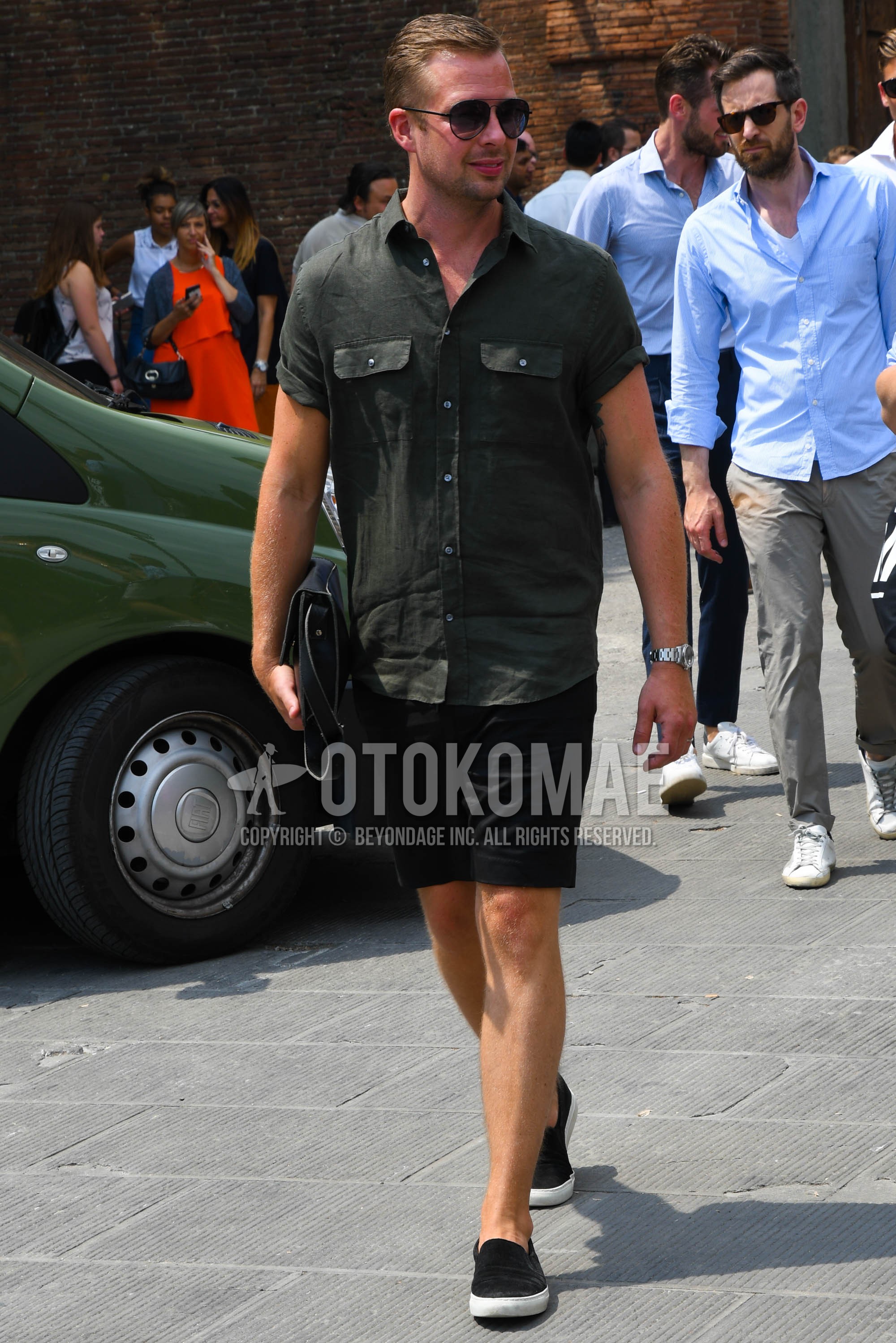 Men's summer outfit with plain sunglasses, olive green plain shirt, black plain short pants, black low-cut sneakers.