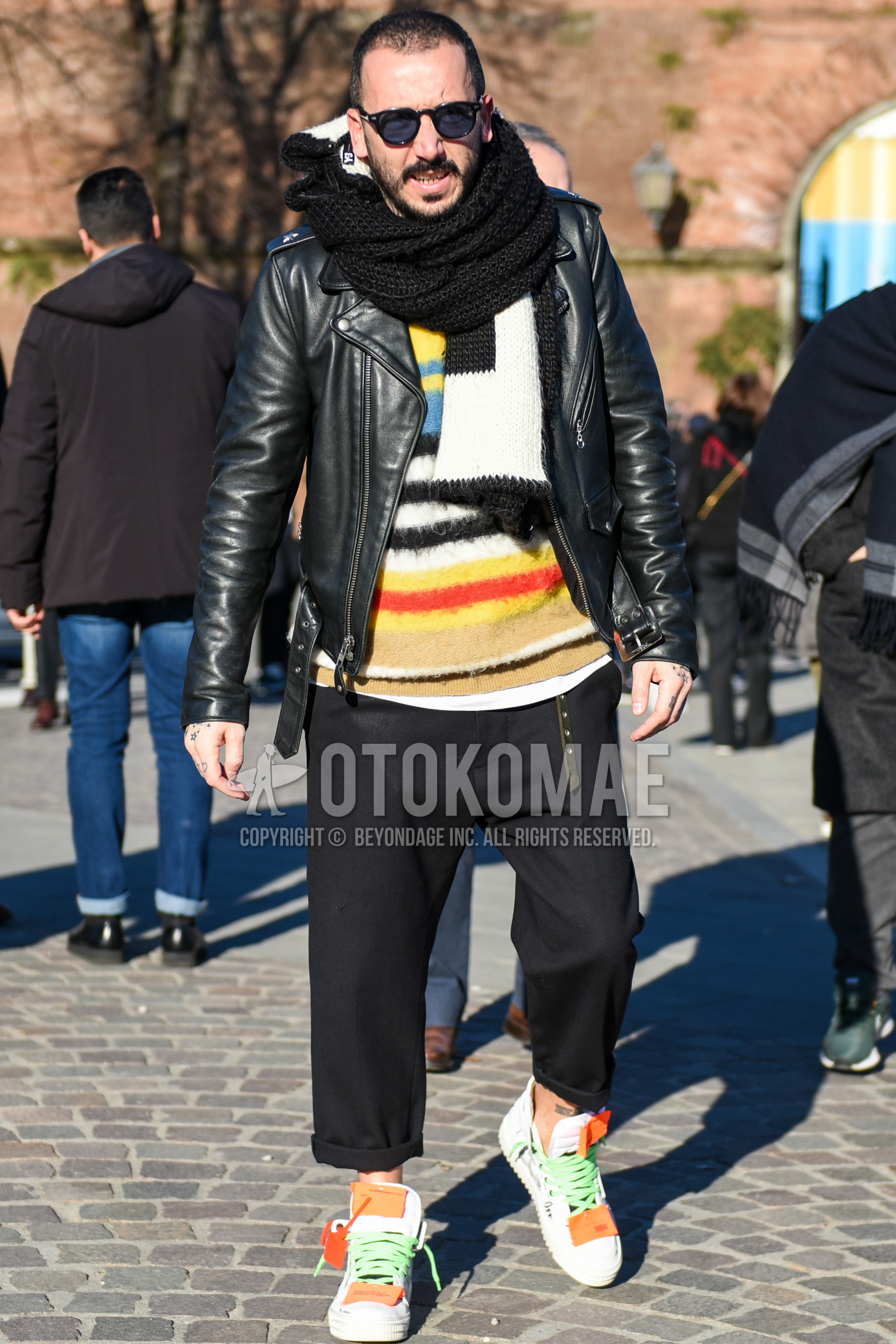 Men's autumn winter outfit with black plain sunglasses, black plain scarf, black plain riders jacket, multi-color tops/innerwear sweater, dark gray plain slacks, dark gray plain cropped pants, white high-cut sneakers.