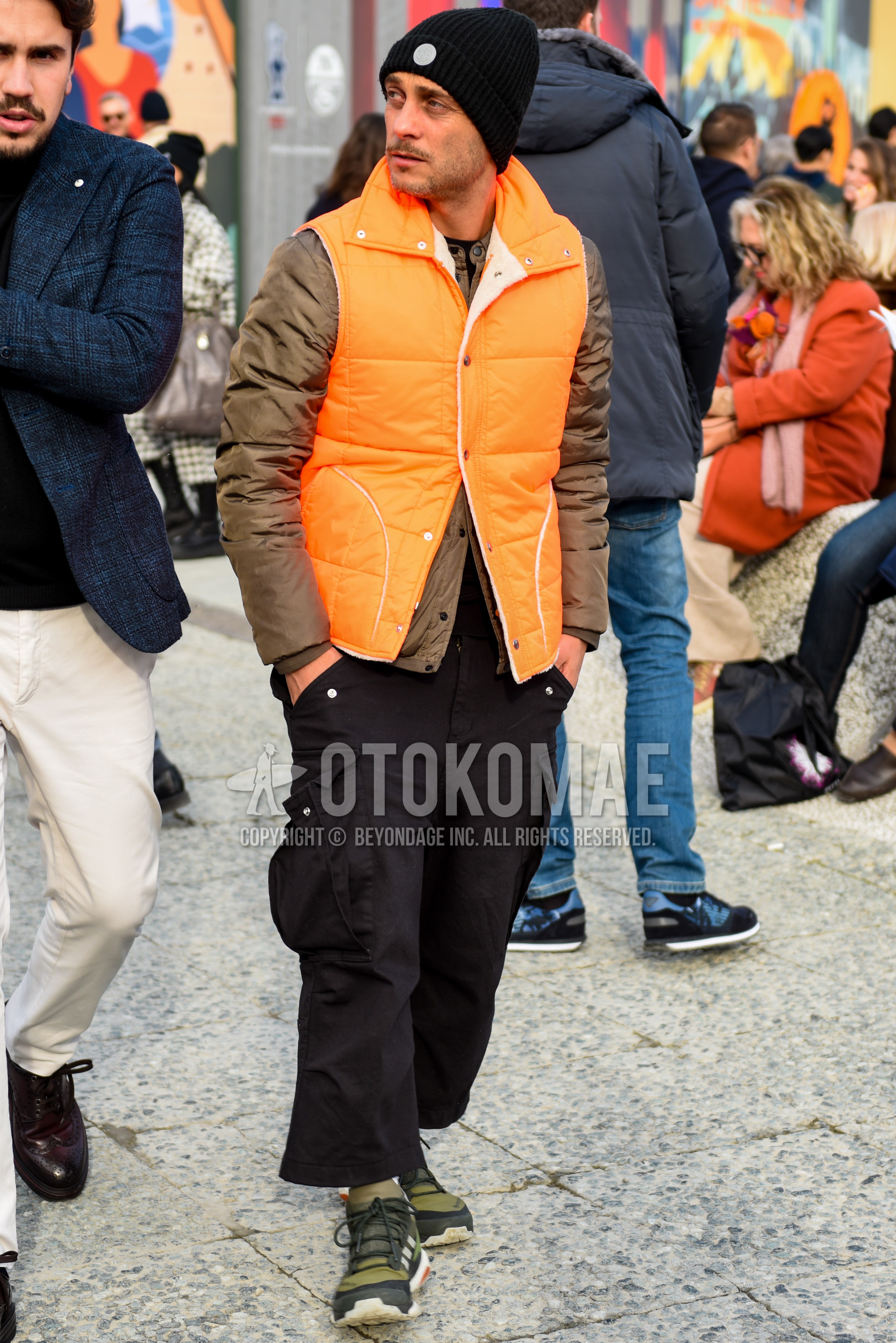 Men's autumn winter outfit with black plain knit cap, orange plain casual vest, brown plain inner down, black plain cropped pants, black plain cargo pants, olive green high-cut sneakers.